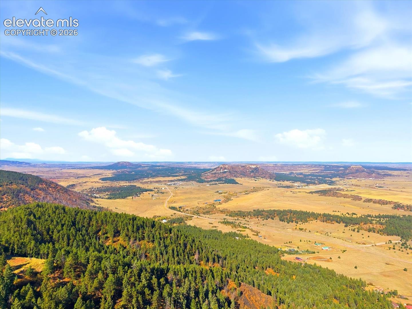 Expansive regional landscape featuring rolling terrain, dense evergreen timberland, and distant plateau formations