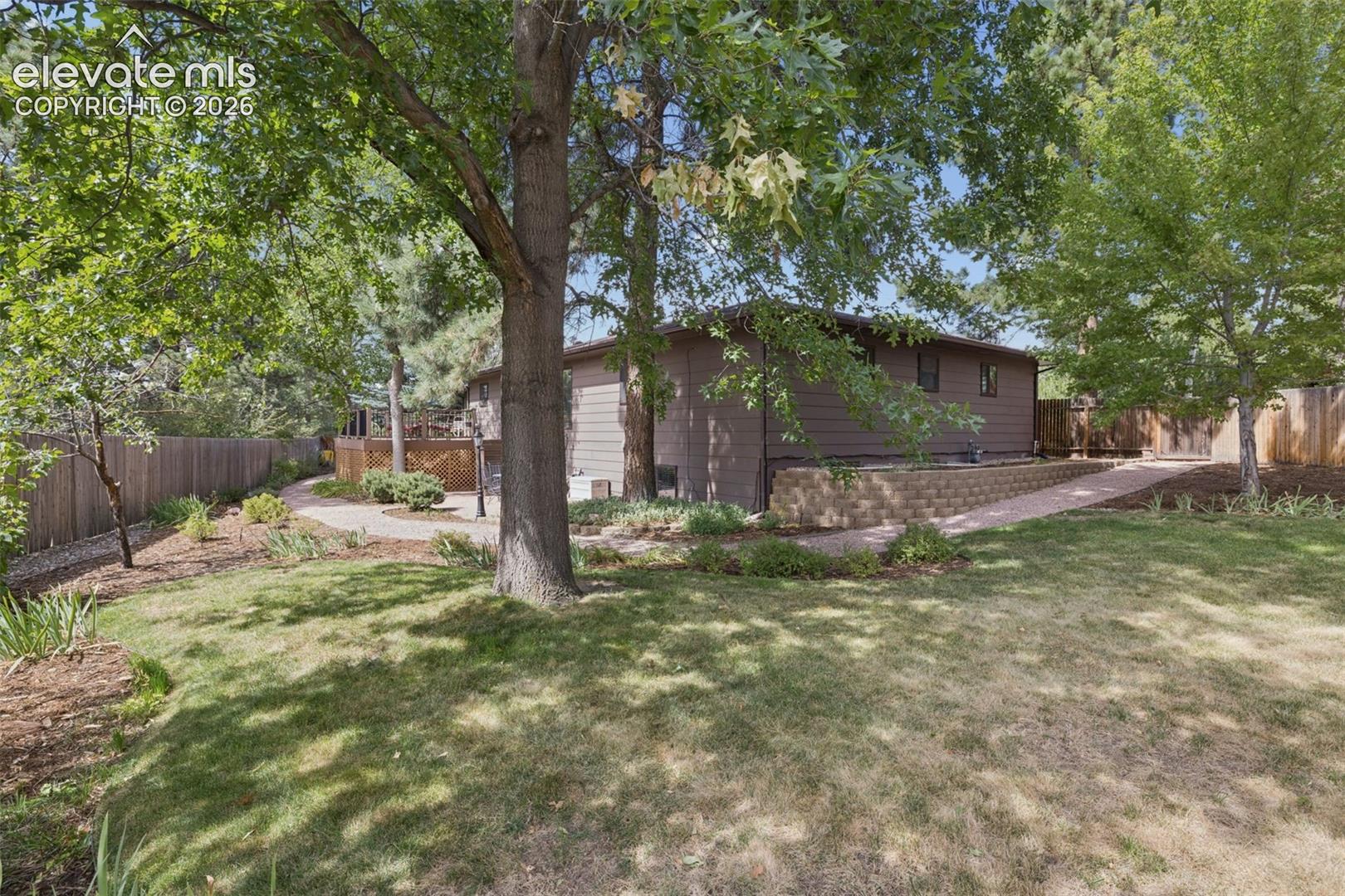 Exterior landscape featuring tiered concrete block retaining walls, mature pine trees and gravel walkway