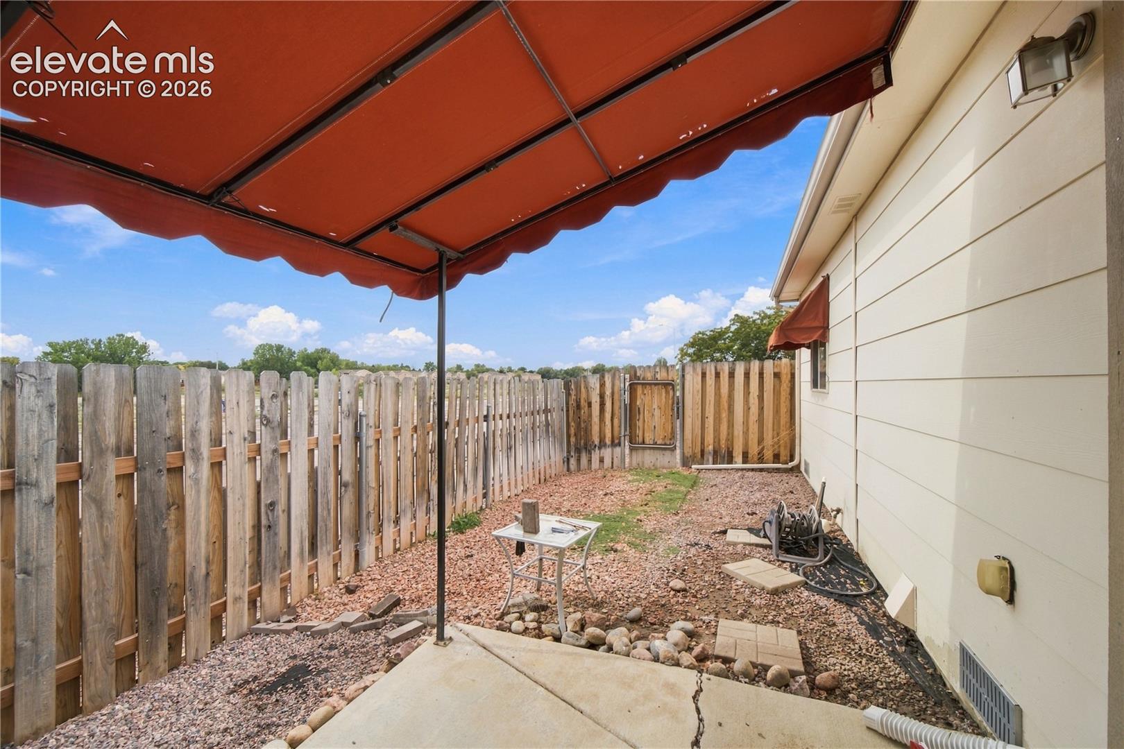 Patio with a retractable awning, wood privacy fencing, and exterior wall lighting