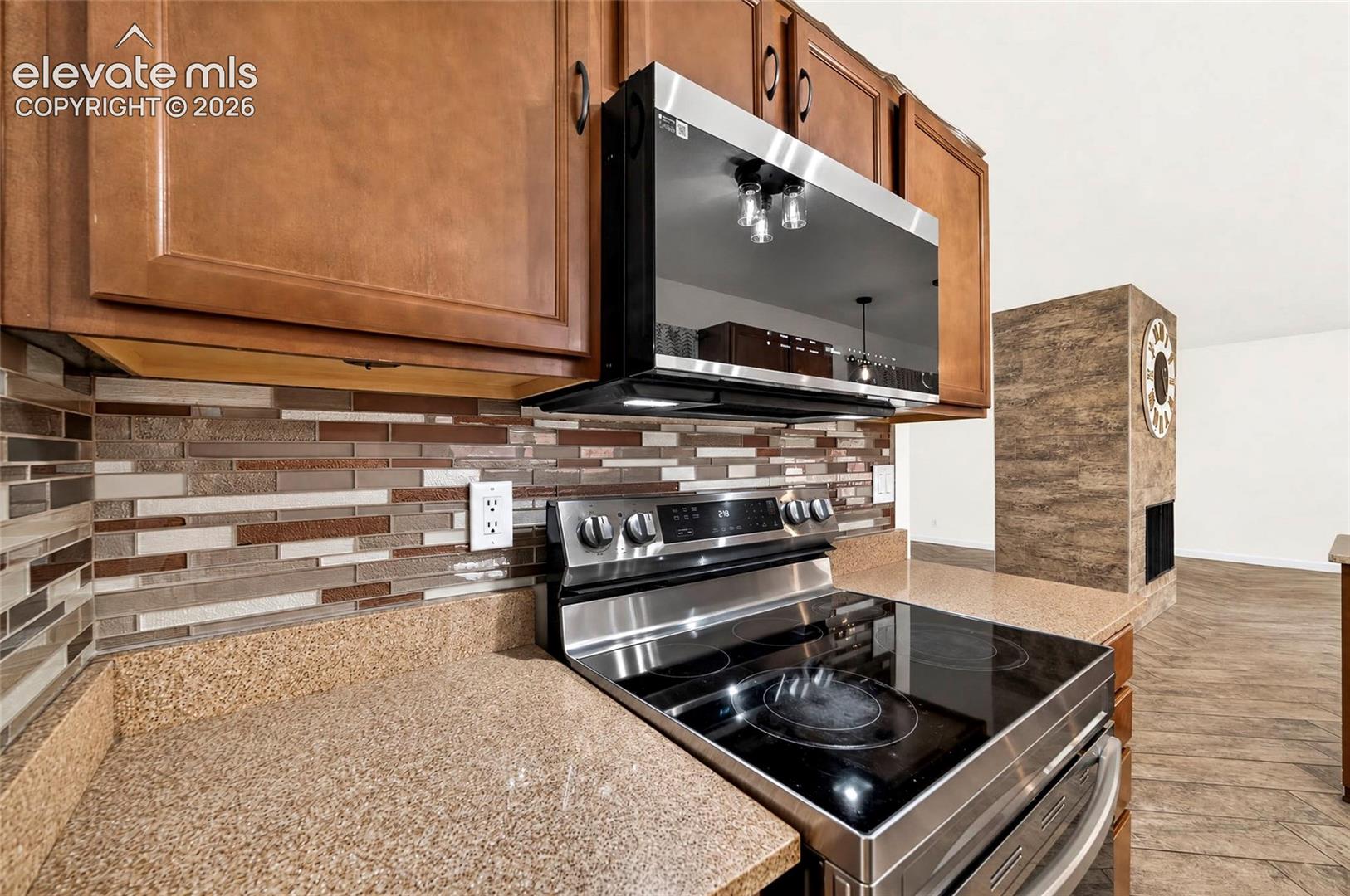 Kitchen featuring warm-toned wood cabinetry, stone-composite countertops, and multi-tonal glass tile backsplash