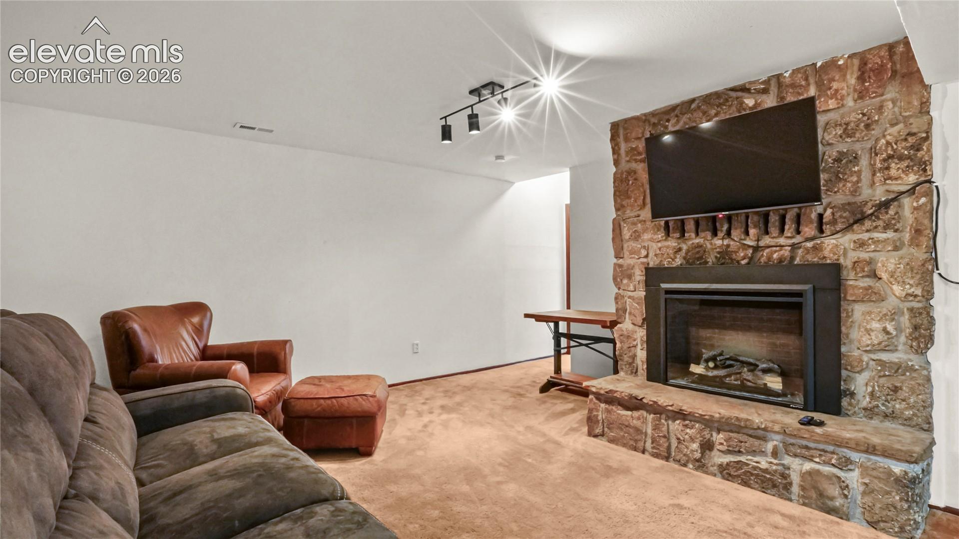 Stone-clad fireplace with a hearth, mounted TV, carpet