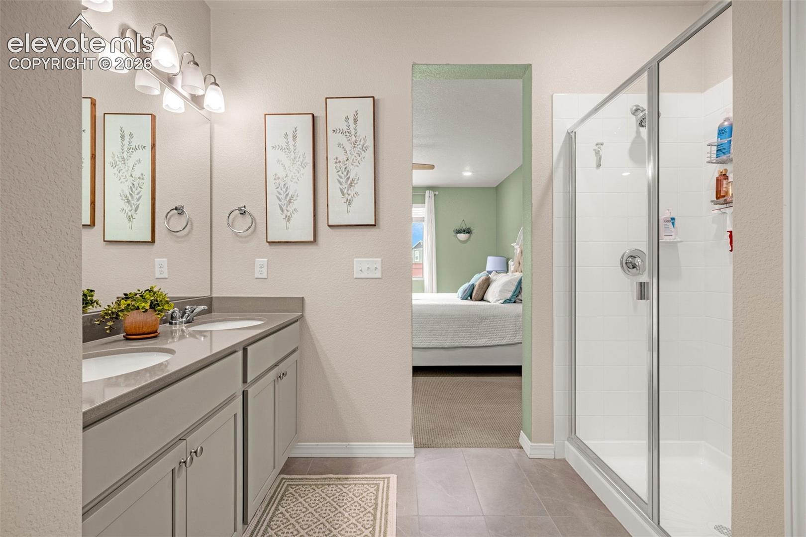 Dual sink vanity with stone-finish countertop, separate glass-enclosed shower, and tile flooring
