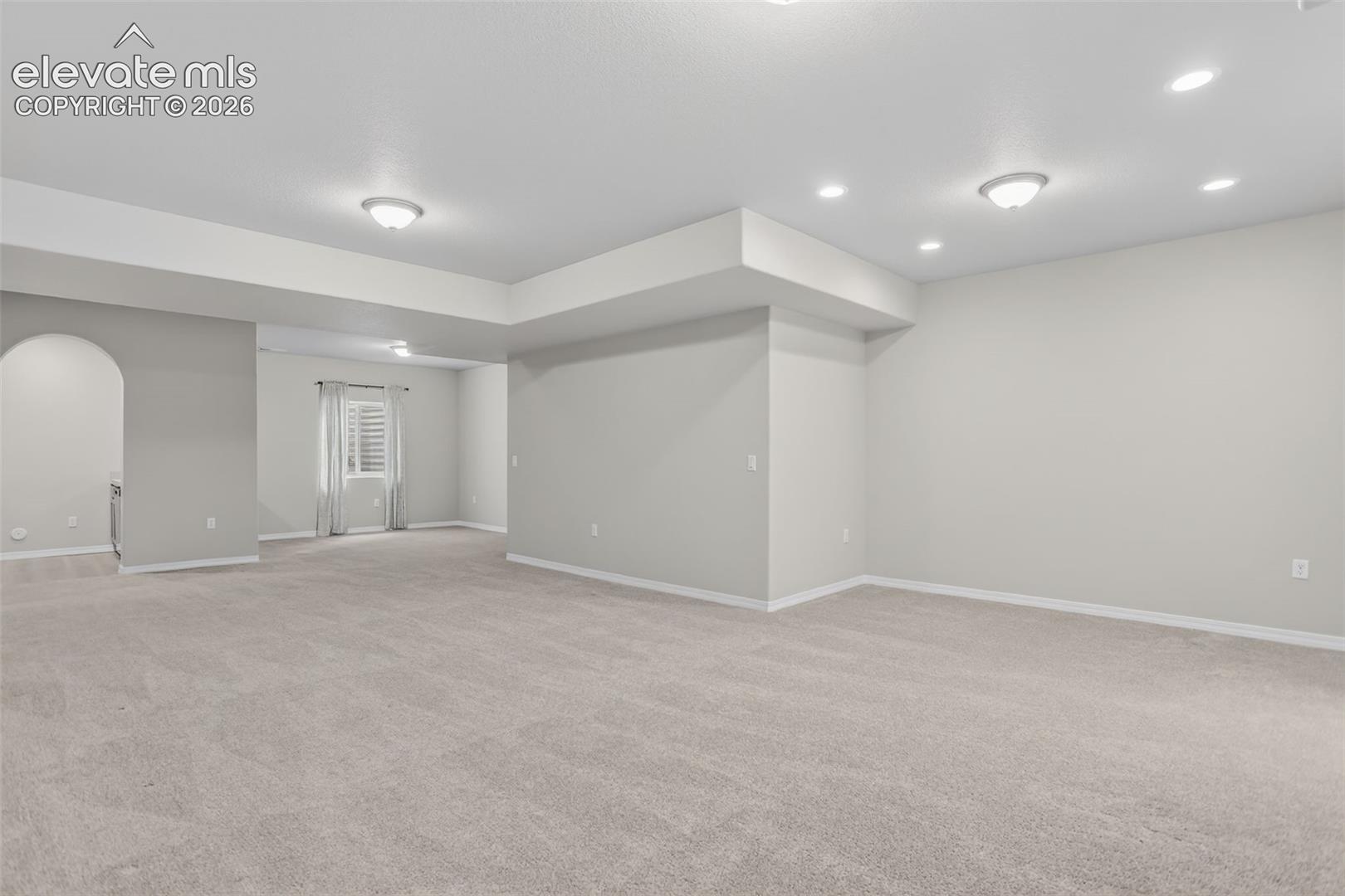 Spacious room featuring light gray carpeting, neutral wall finishes, recessed lighting, and an arched entry