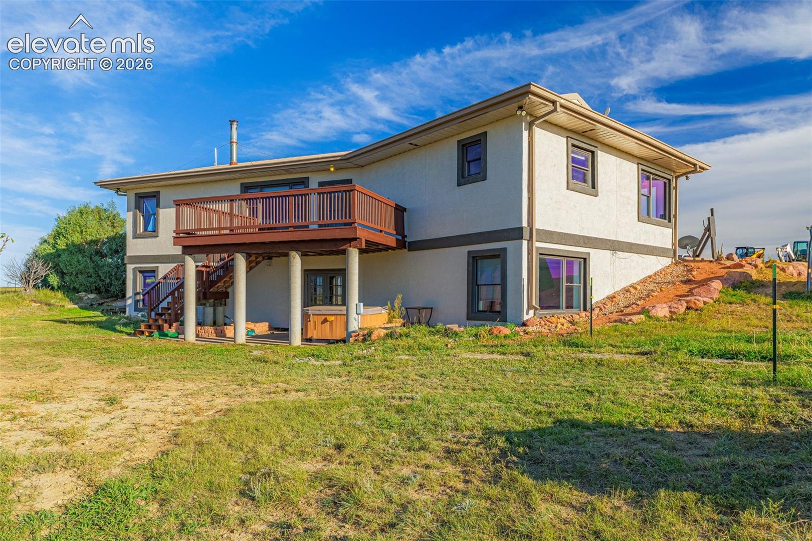 Multi-level exterior with stucco finish, elevated wood deck with railings, and a built-in hot tub