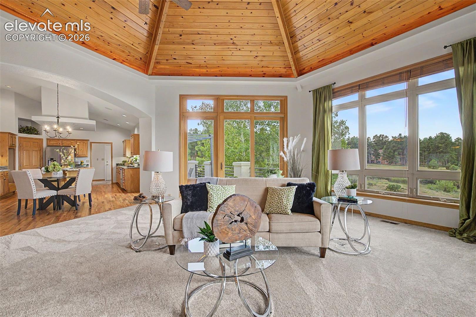 Vaulted wood-paneled ceiling with a central fan, large windows with natural wood frames, and a glass-paneled door