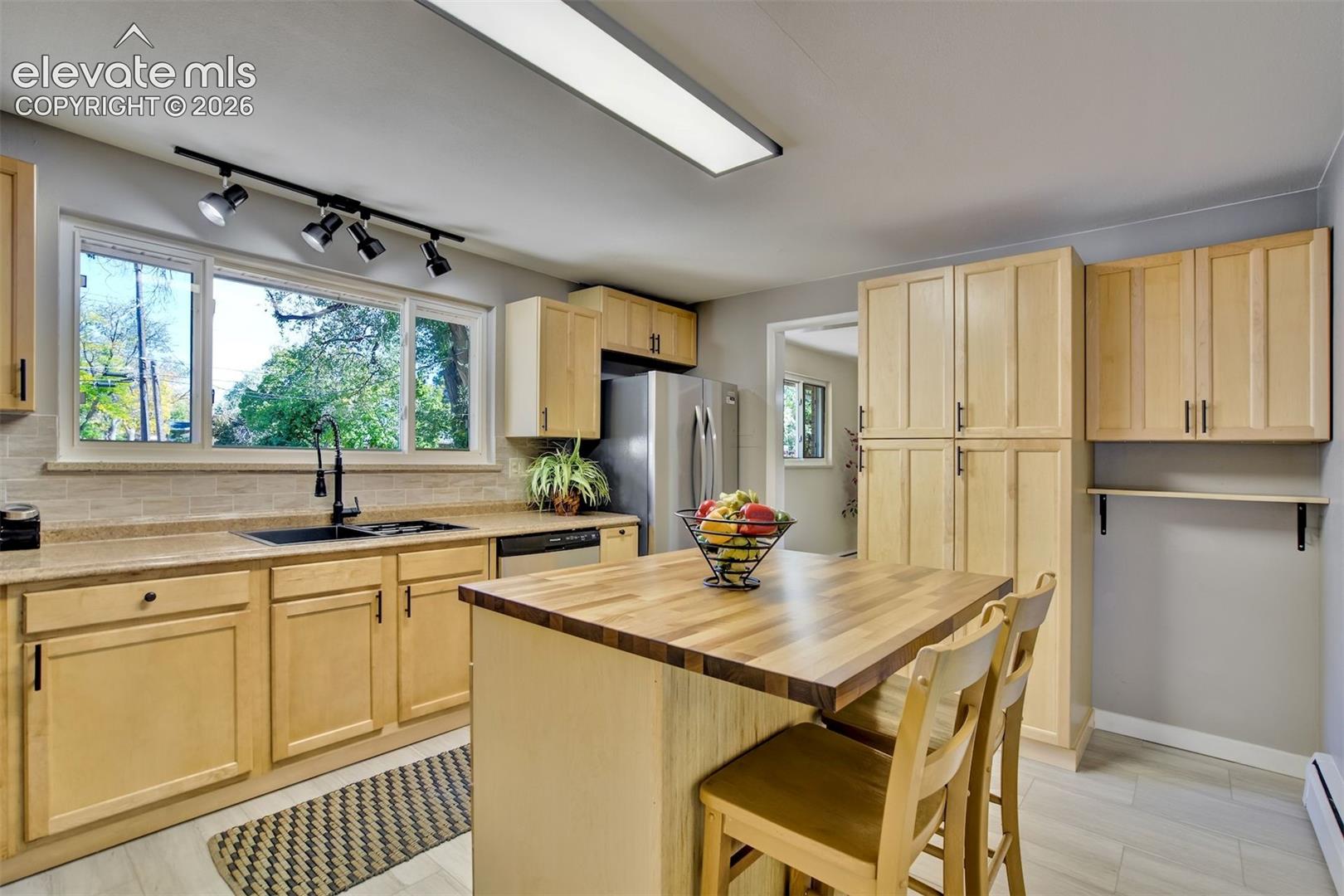 Kitchen featuring light-tone wood cabinetry, central island with a wood countertop, integrated stainless steel appliances, horizontal tile backsplash, and matte black plumbing fixtures