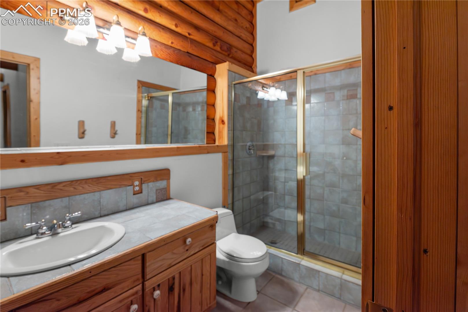 Full bathroom featuring vanity, a stall shower, tile patterned flooring, and rustic walls