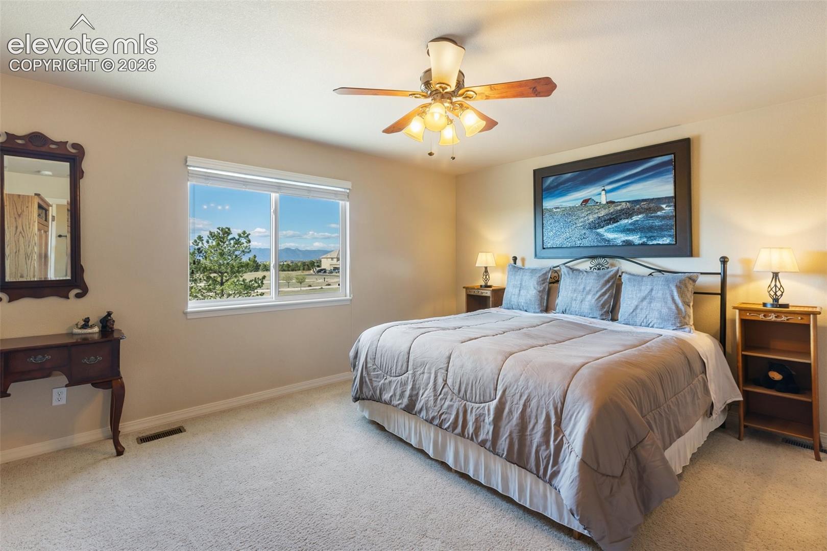 Neutral-toned room featuring wall-to-wall carpeting, a multi-light ceiling fan, and a large window with exterior mountain scenery