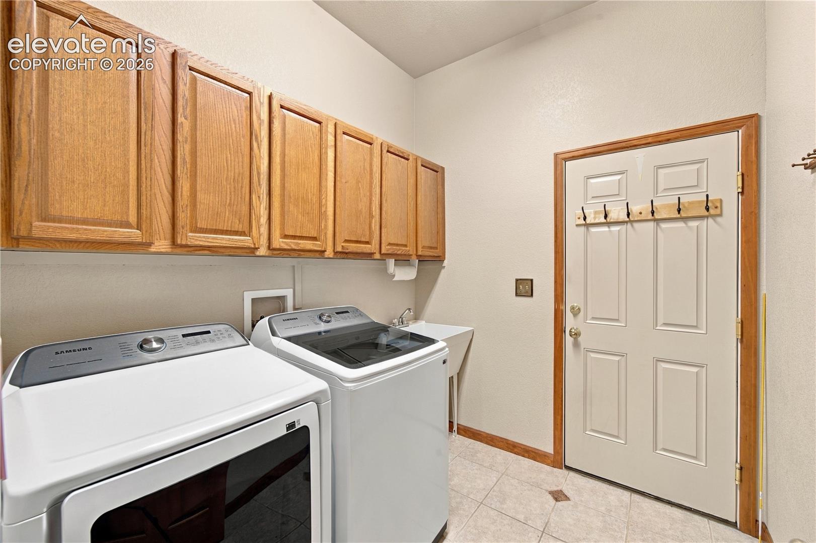 Laundry area featuring shaker-style wooden cabinetry, tile flooring, a utility sink, and a multi-panel exterior door with integrated hardware
