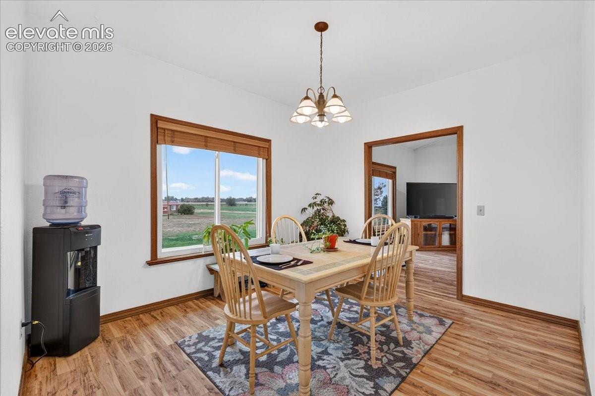 Dining area featuring wood-finish flooring, a multi-light chandelier, and large window with wood trim