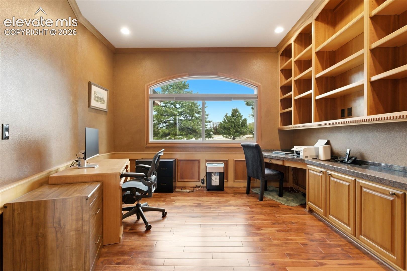 Wood-finish flooring with built-in cabinetry, an arched window, and custom shelving
