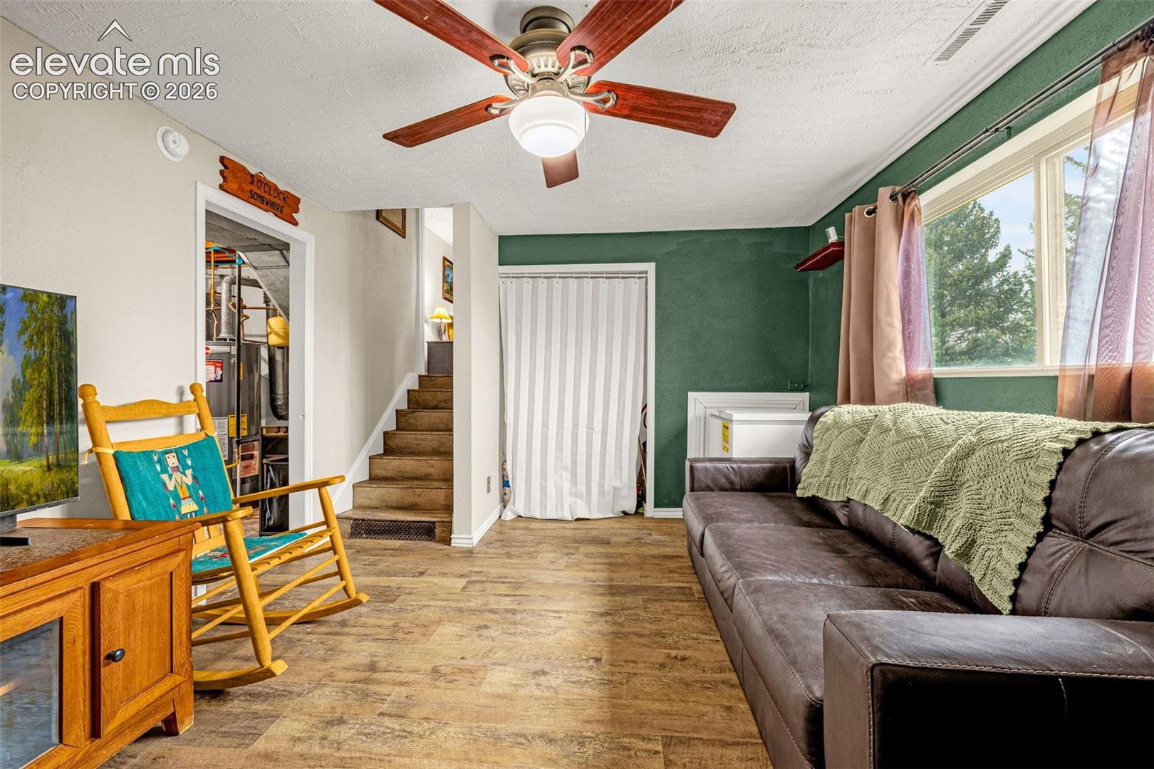Wood-finish flooring, ceiling fan with integrated lighting, accent wall, and wood-tread staircase