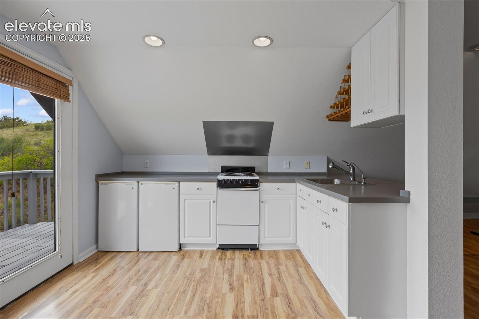 ADU kitchen with range, two mini fridges, sink, white cabinetry, and walk-out to deck.