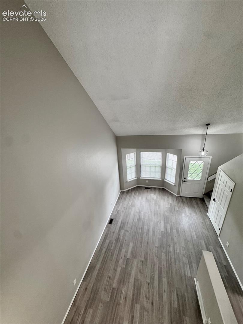 Living area with wood-finish flooring, bay windows, and a hanging pendant light fixture