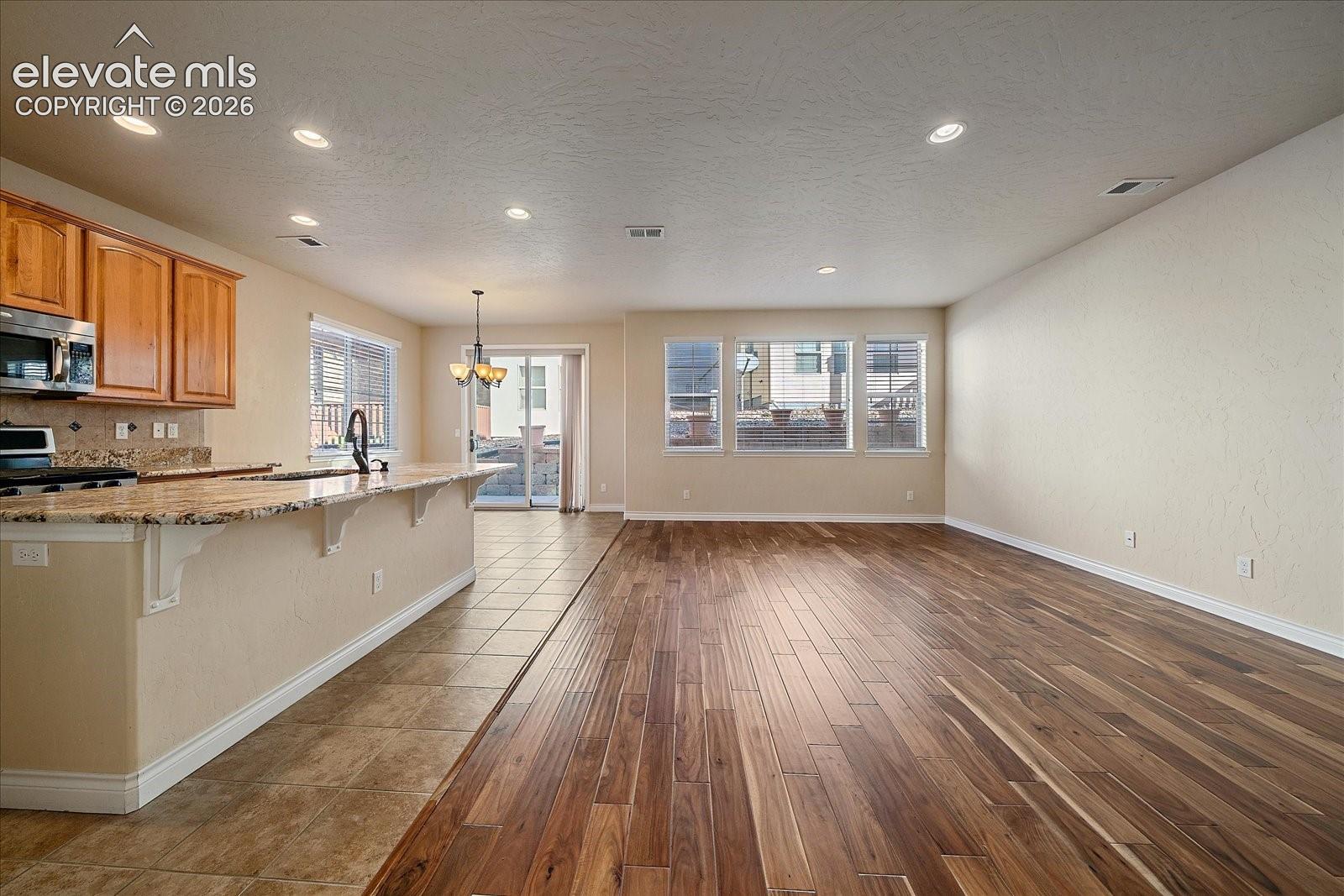 Open-concept interior featuring wood-finish flooring, a kitchen island with stone-finish countertops, recessed lighting, and a sliding glass door