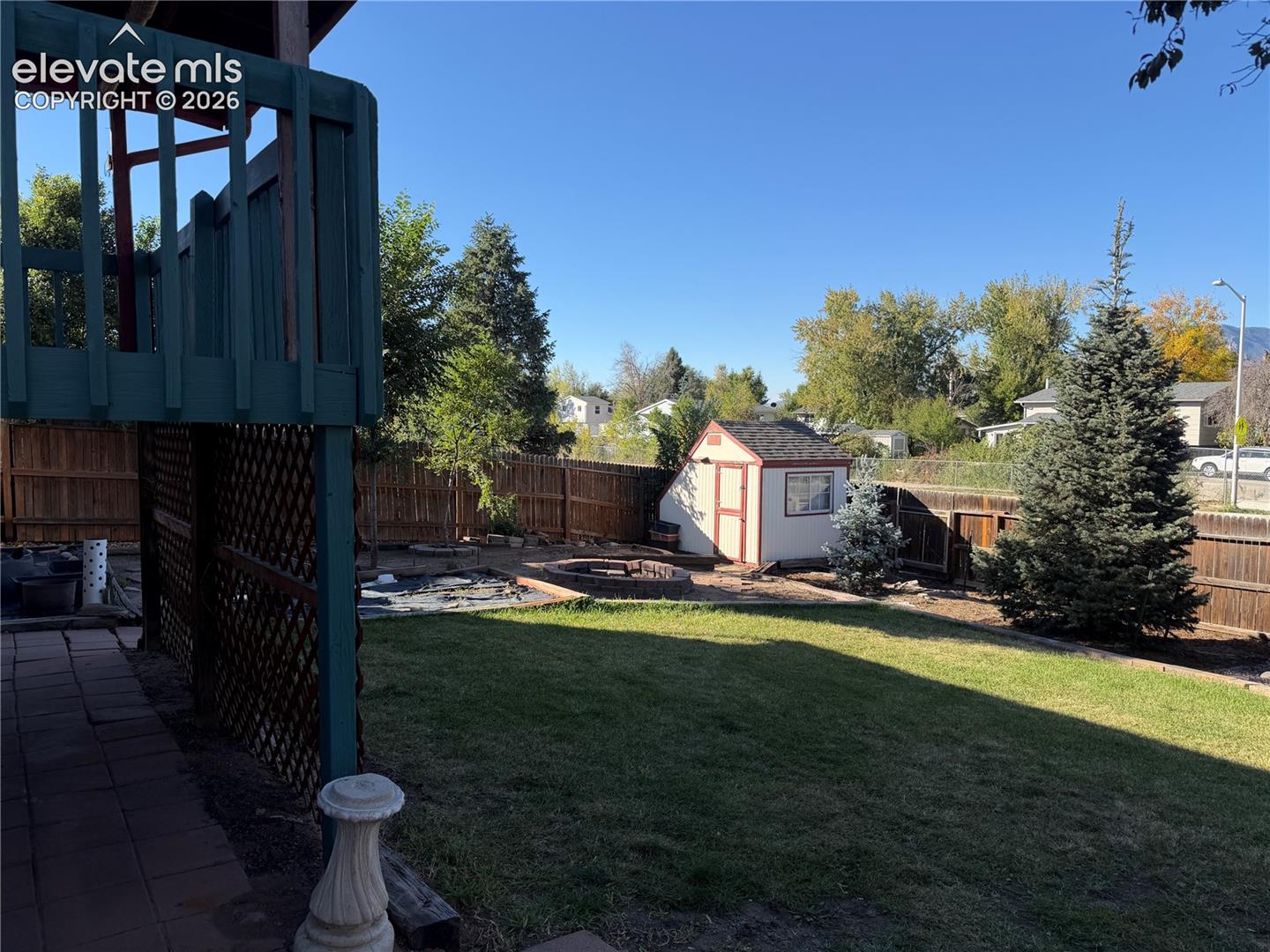 Fenced backyard featuring a manicured lawn, a detached storage shed, a stone-bordered fire pit, and a tiled patio area