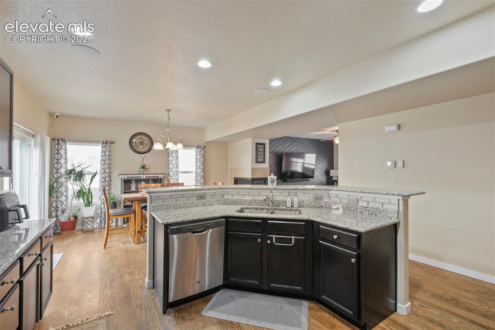Kitchen island featuring dark cabinetry, stainless steel dishwasher, an undermount sink, and light-toned countertops