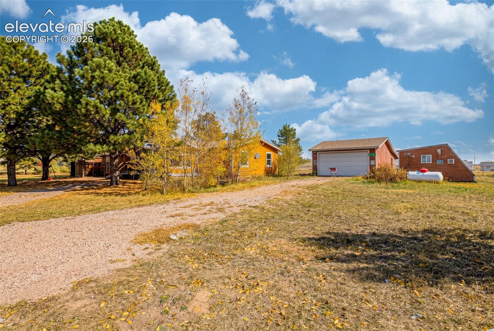 Gravel driveway, detached 2-car garage, mature trees, and open acreage