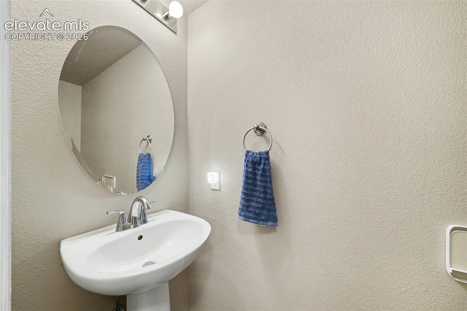 Oval wall-mounted mirror, pedestal sink with a dual-handle metal faucet, and circular metal towel ring