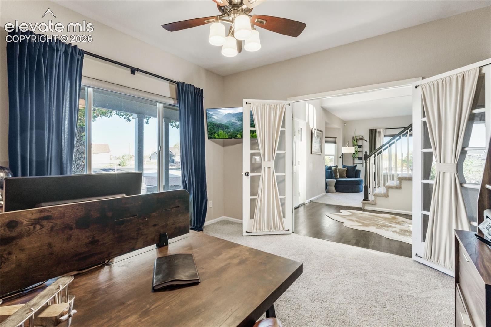 Multi-pane glass French doors, ceiling fan with integrated lighting, neutral carpeted flooring, and large window with exterior exposure