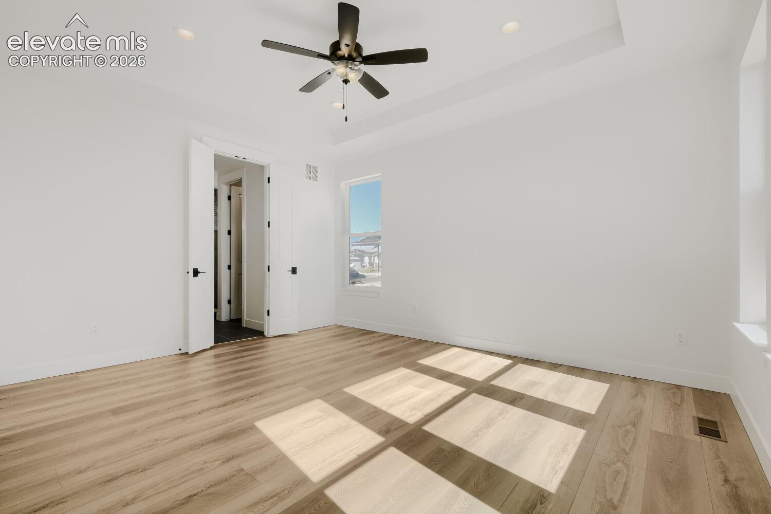 Wood-finish flooring, white walls, tray ceiling, recessed lighting, and a ceiling fan with light
