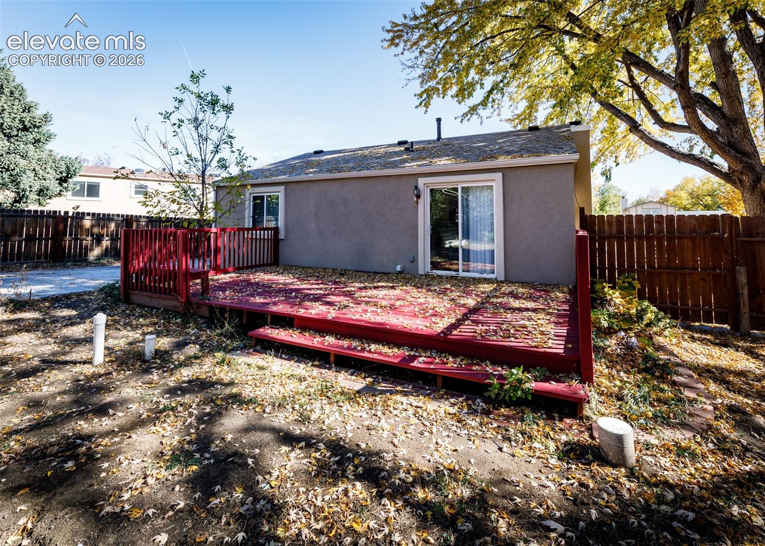 Raised wooden deck featuring red-tone finish, perimeter railings, and integrated step, enclosed by wooden privacy fencing