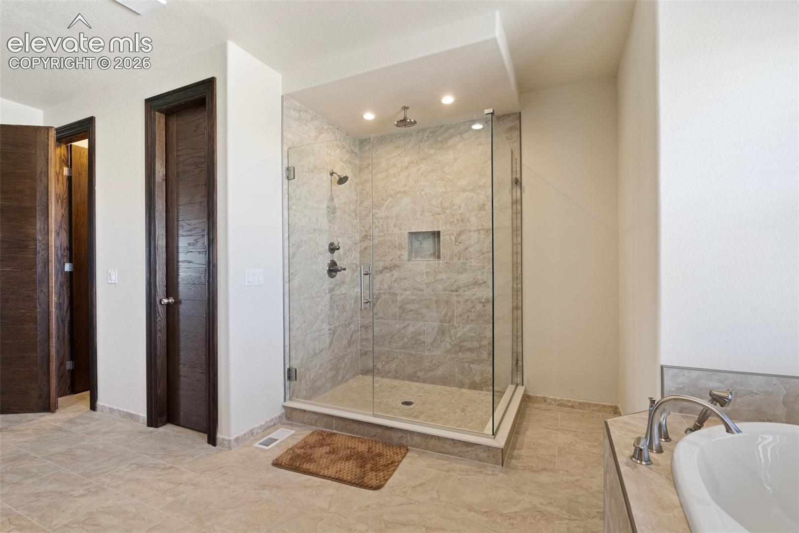 Glass-enclosed shower with a tiled surround and built-in niche, featuring dual shower heads and a bench