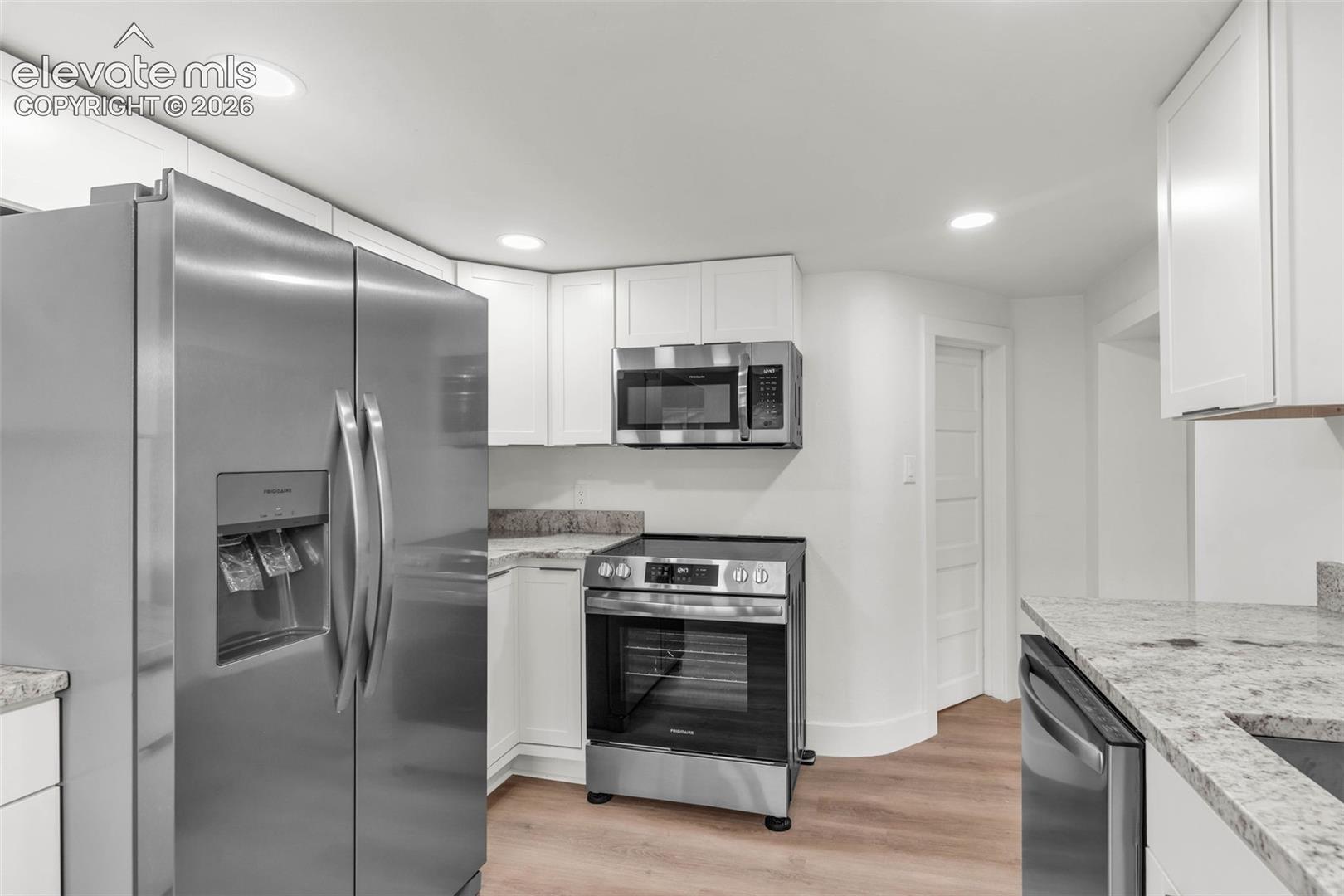 Kitchen featuring white shaker-style cabinetry, light-toned stone-finish countertops, stainless steel appliances, and recessed lighting