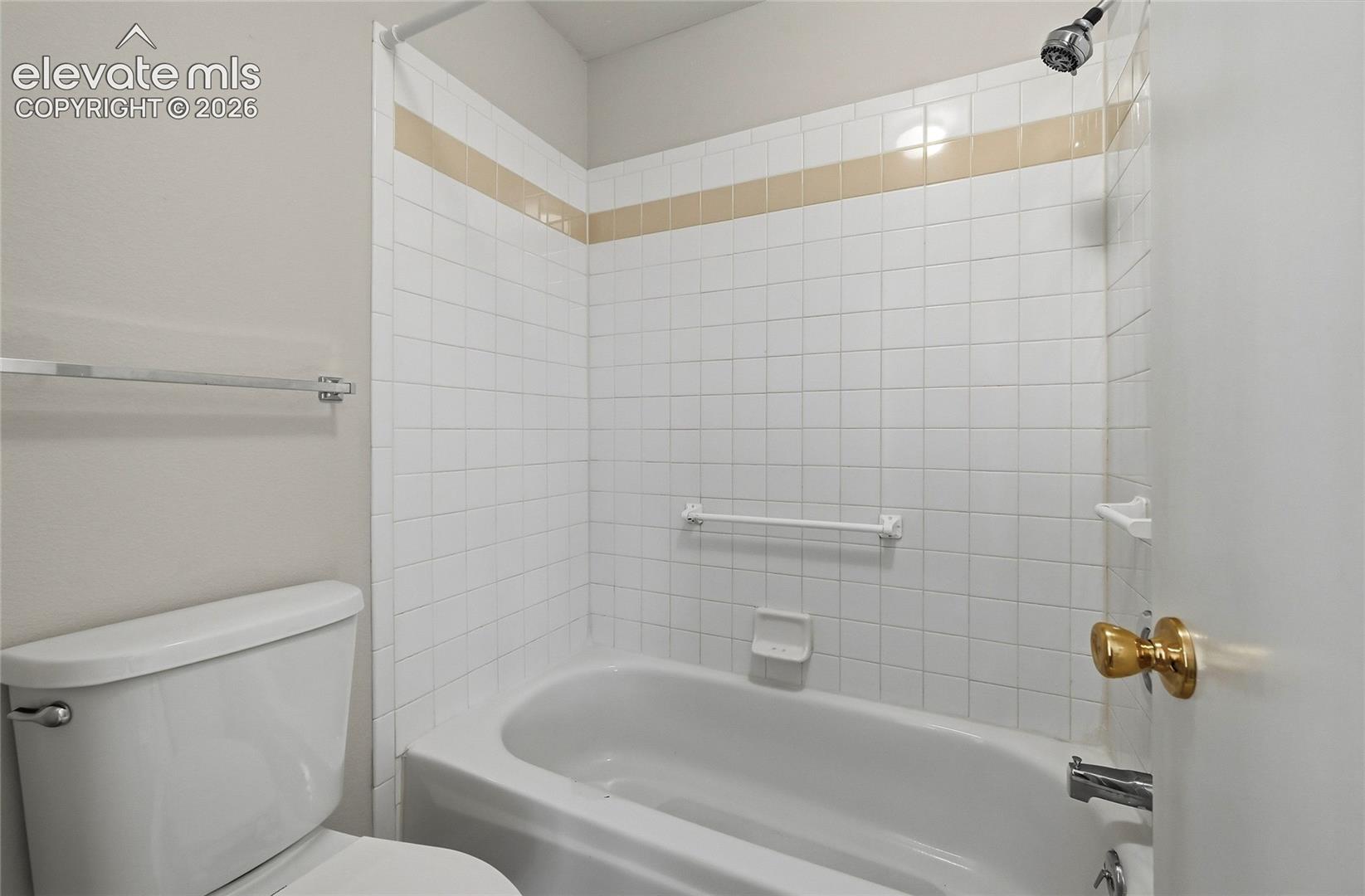 Bathtub with white square wall tiles featuring a contrasting accent band, integrated soap dish, and wall-mounted shower head