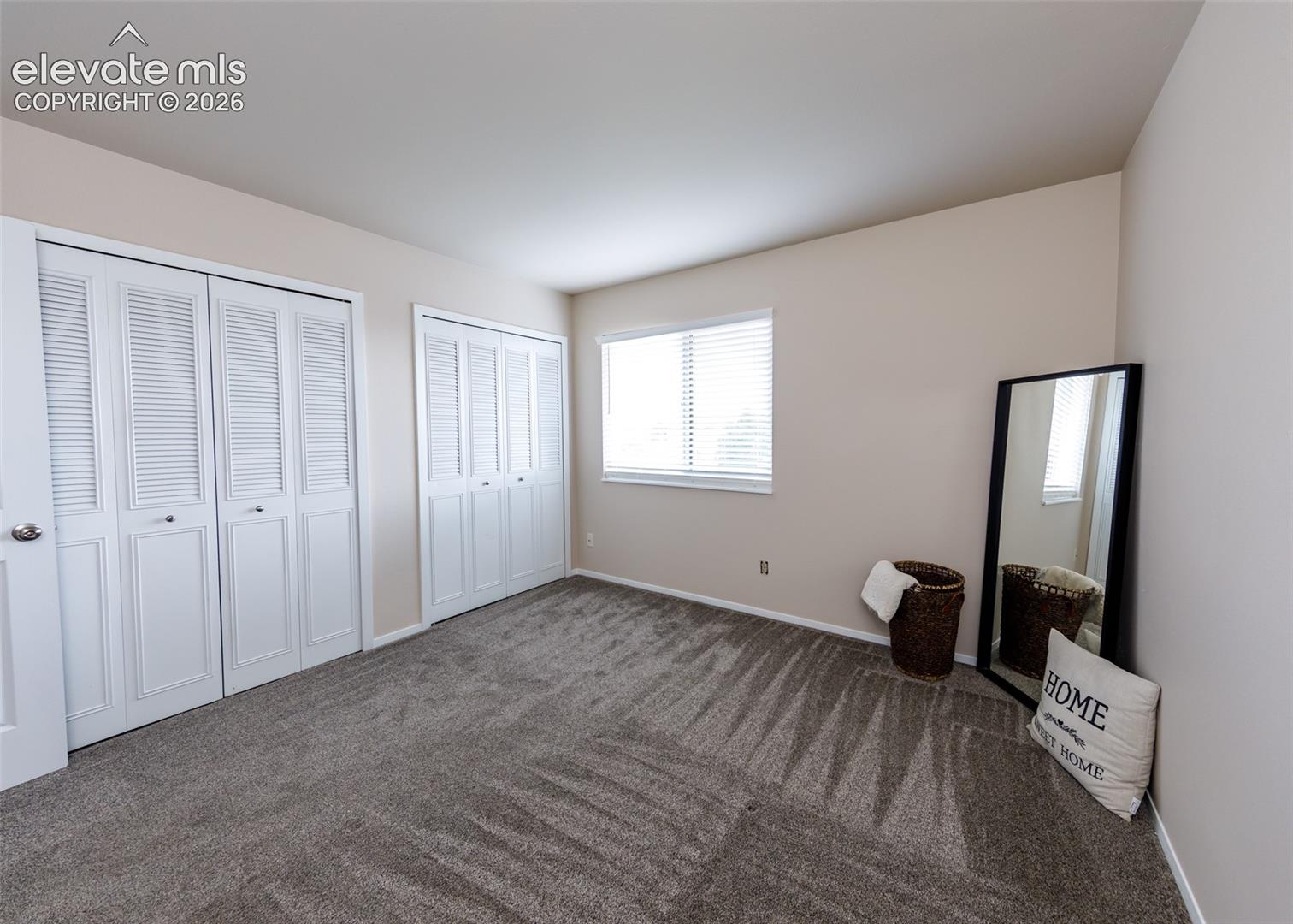 Neutral wall paint, two sets of louvered bi-fold closet doors, wall-to-wall carpeting, and a window with blinds