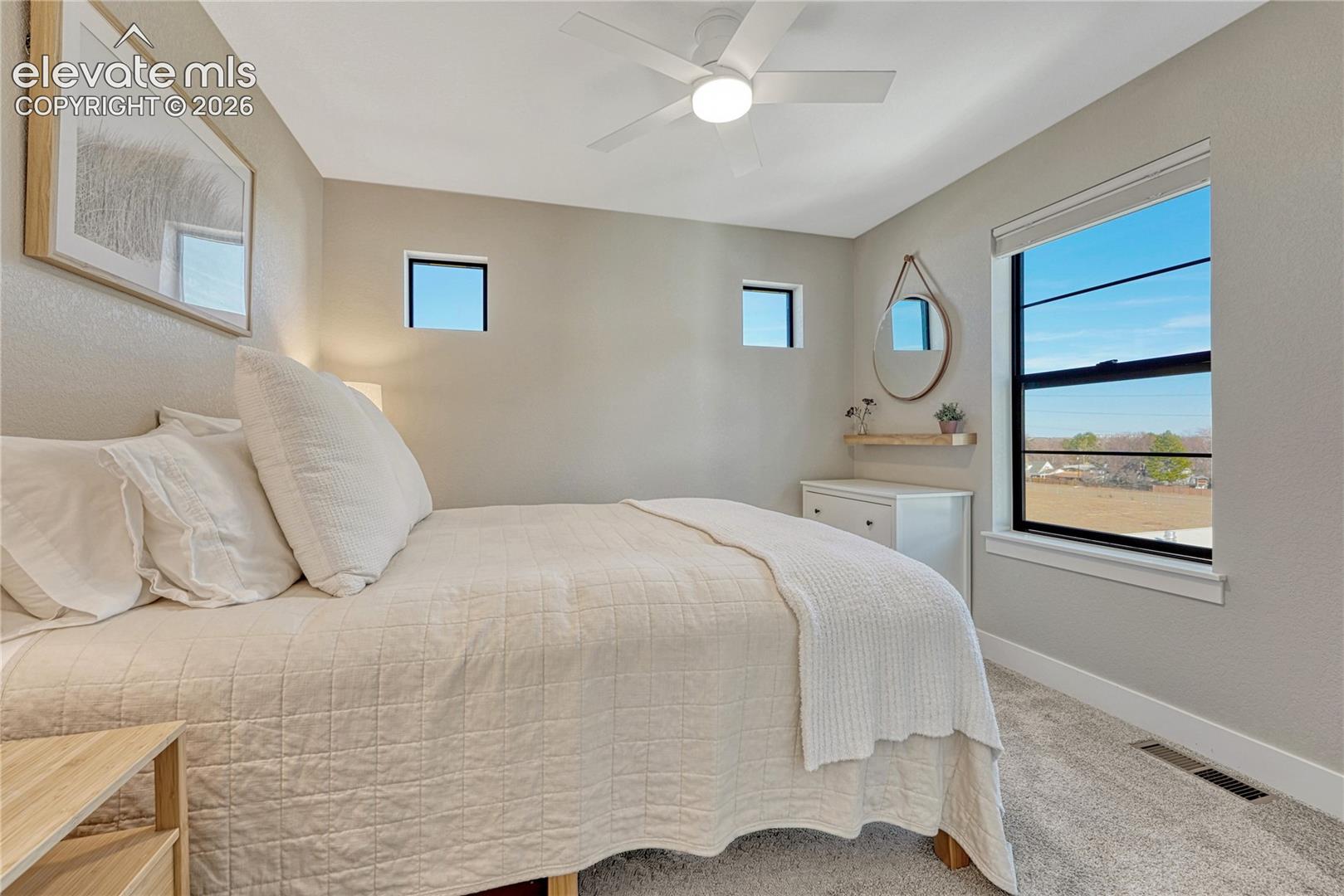 Neutral-toned room featuring neutral carpeting, dual square accent windows, large picture window with black framing, and a ceiling-mounted light fixture with integrated fan