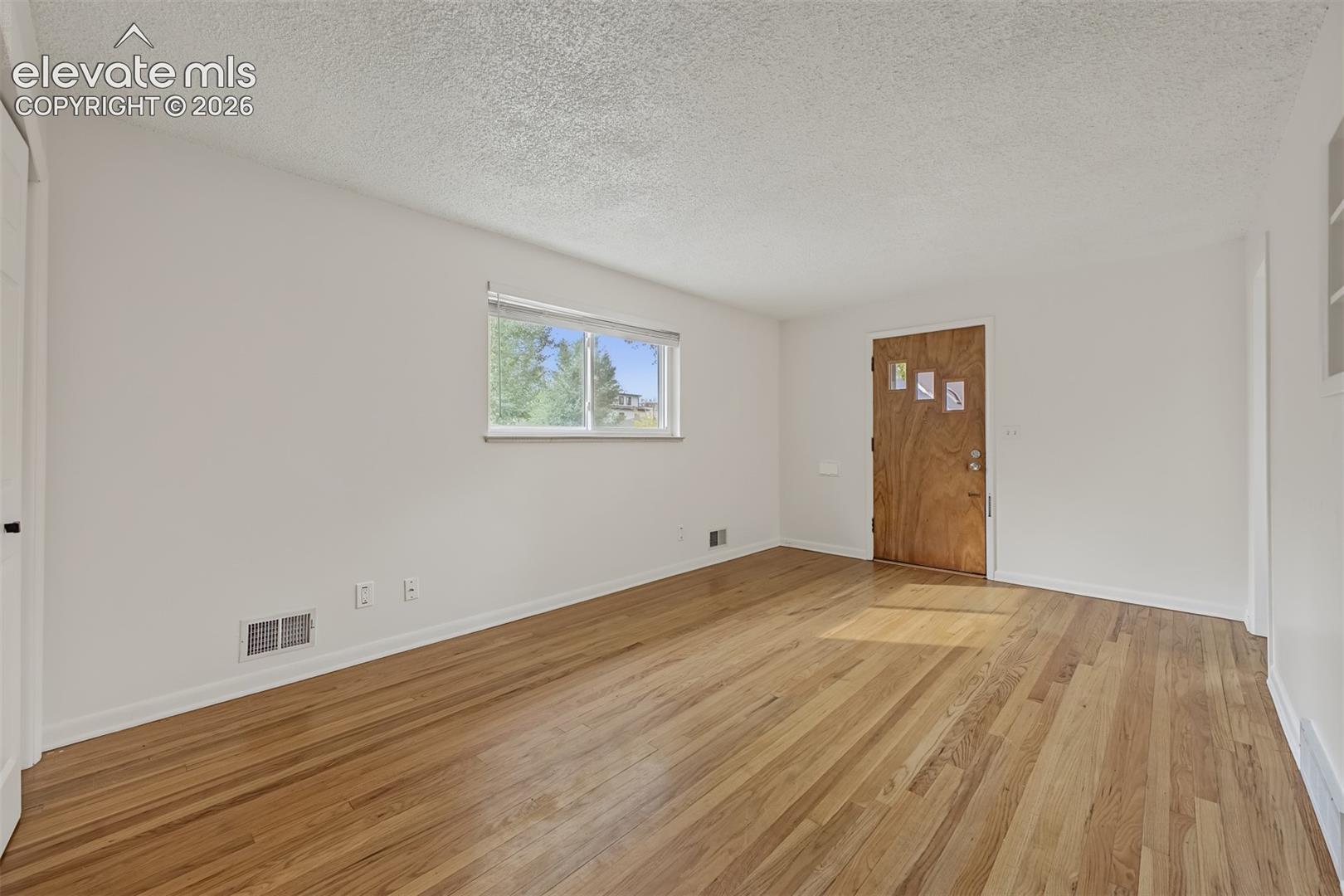 Interior space featuring wood-finish flooring, textured ceiling, single-pane window, and a wood-panel entry door