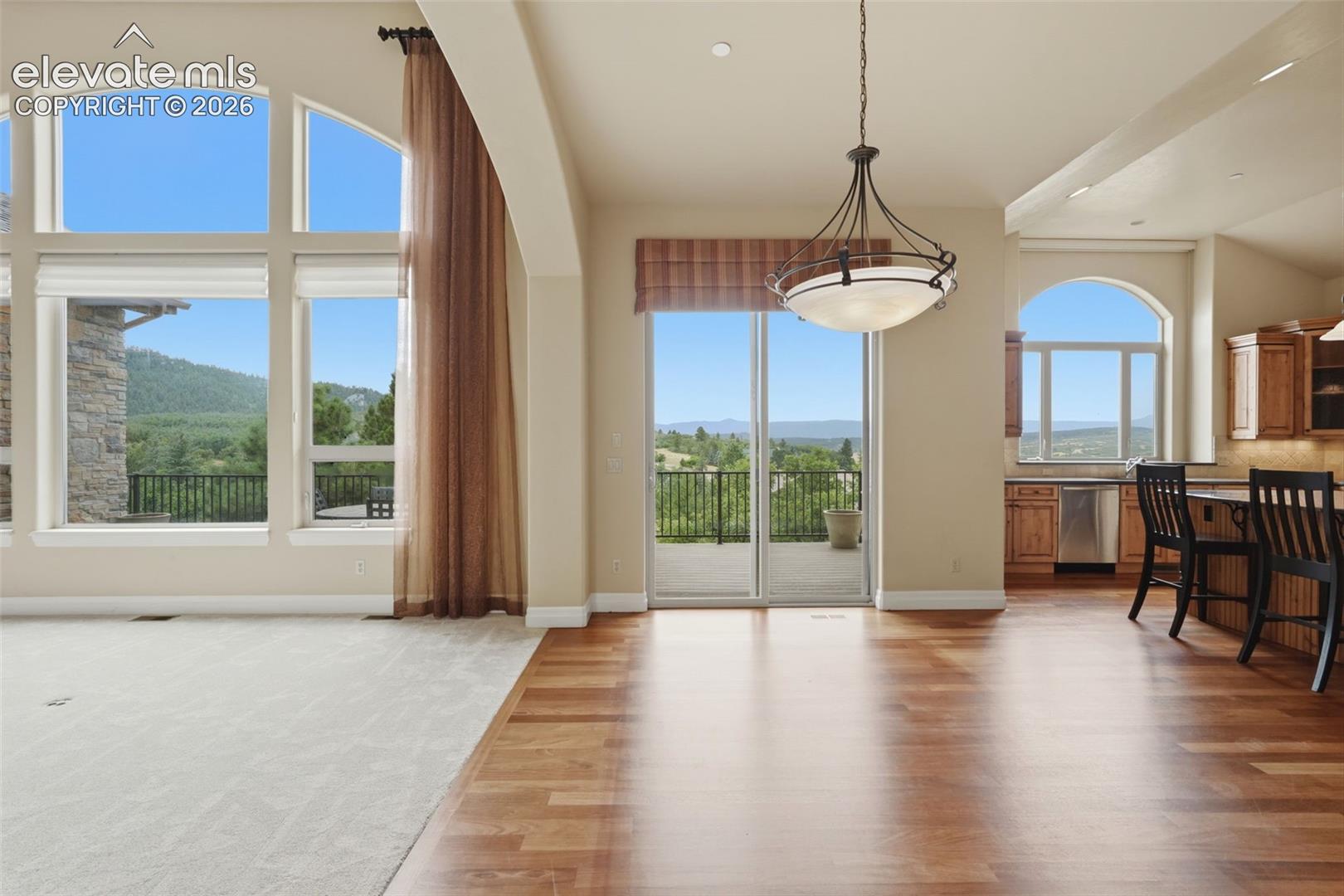 Spacious open-concept living area featuring large arched windows, wood-finish flooring, and a sliding glass door leading to an outdoor balcony