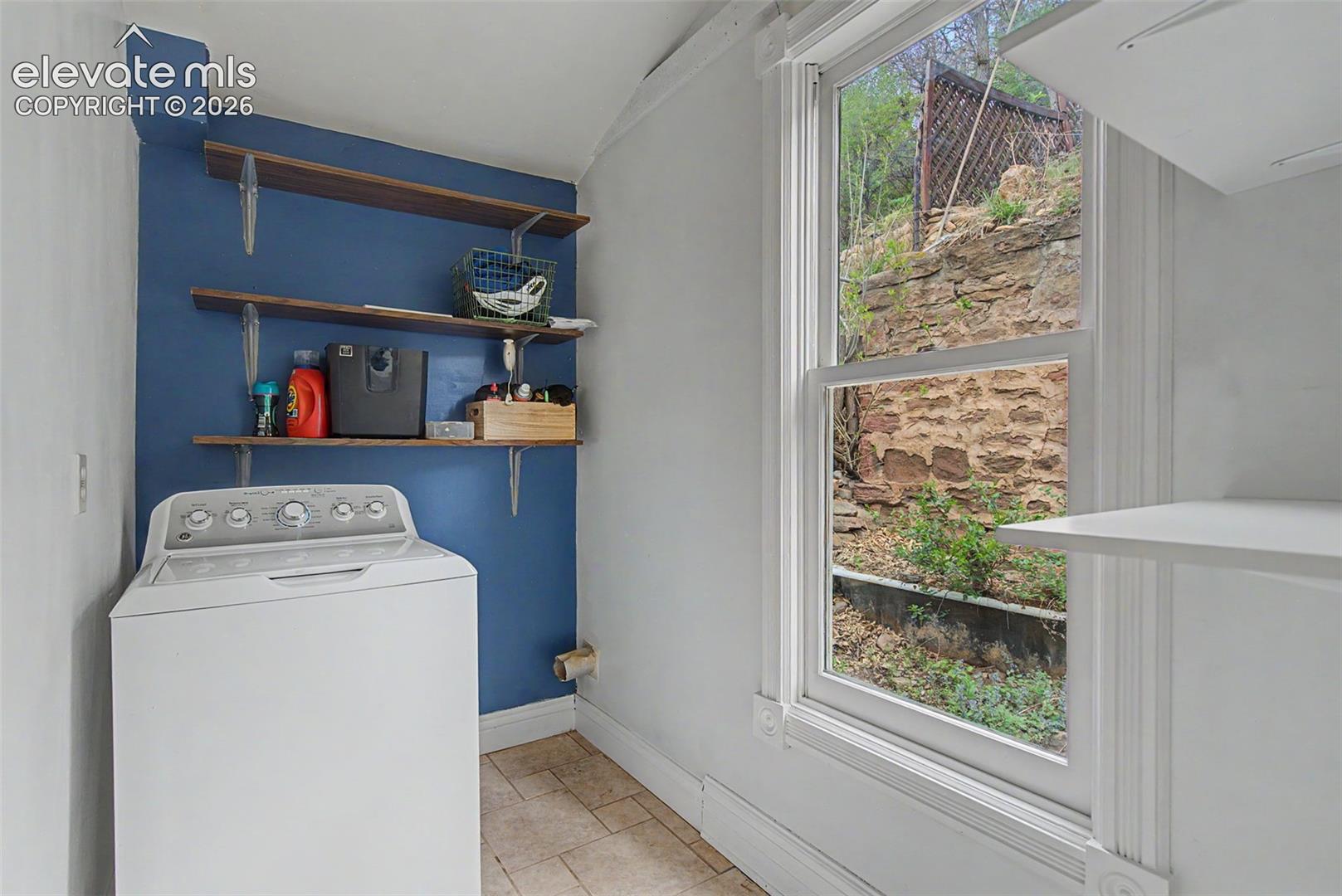 Dedicated laundry space featuring a white top-load washing machine, shelving, and tiled flooring