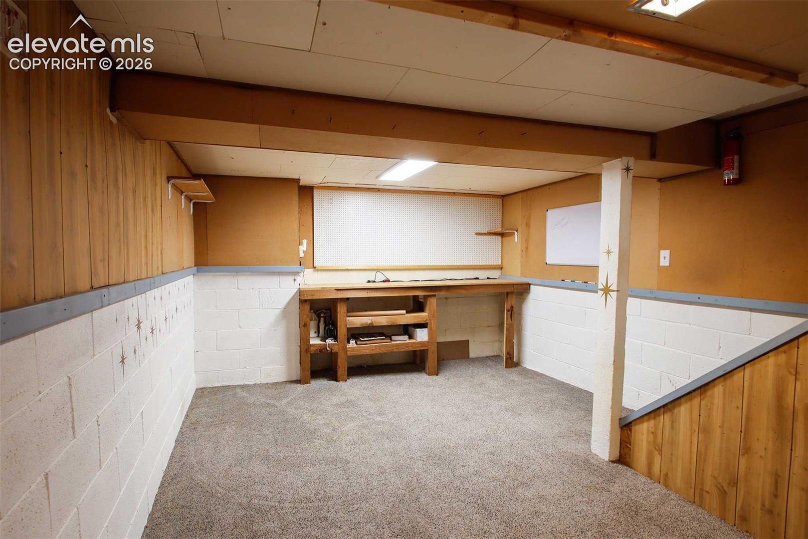 Carpeted floor, wood paneling, painted, non-conforming concrete block walls, built-in wooden workbench, and exposed ceiling beams