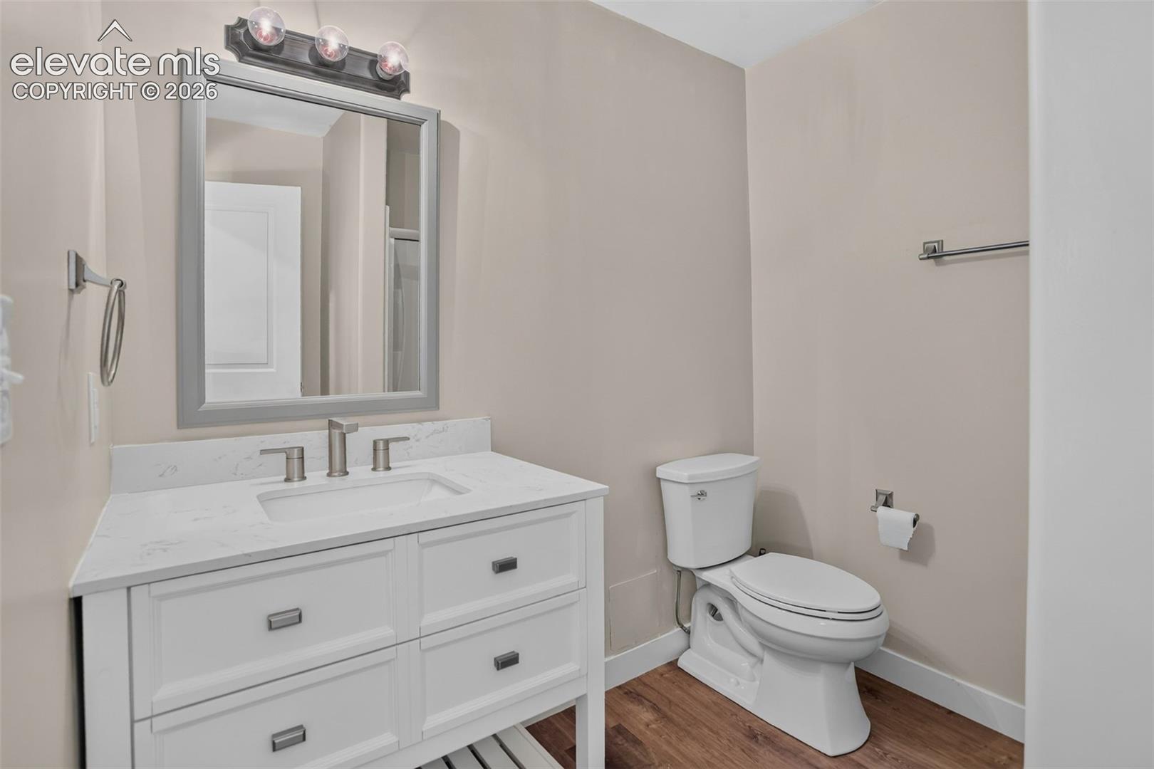 White vanity with integrated sink, brushed nickel faucet, framed mirror, and wood-finish flooring