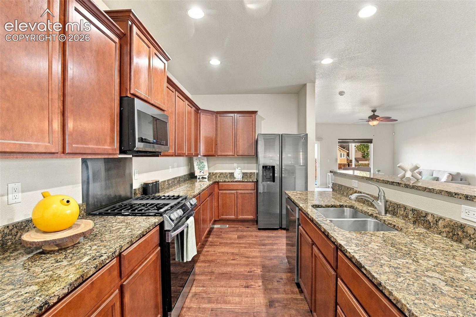 Kitchen featuring wood cabinetry, stone-surface countertops, wood-finish flooring, stainless steel appliances, and recessed lighting