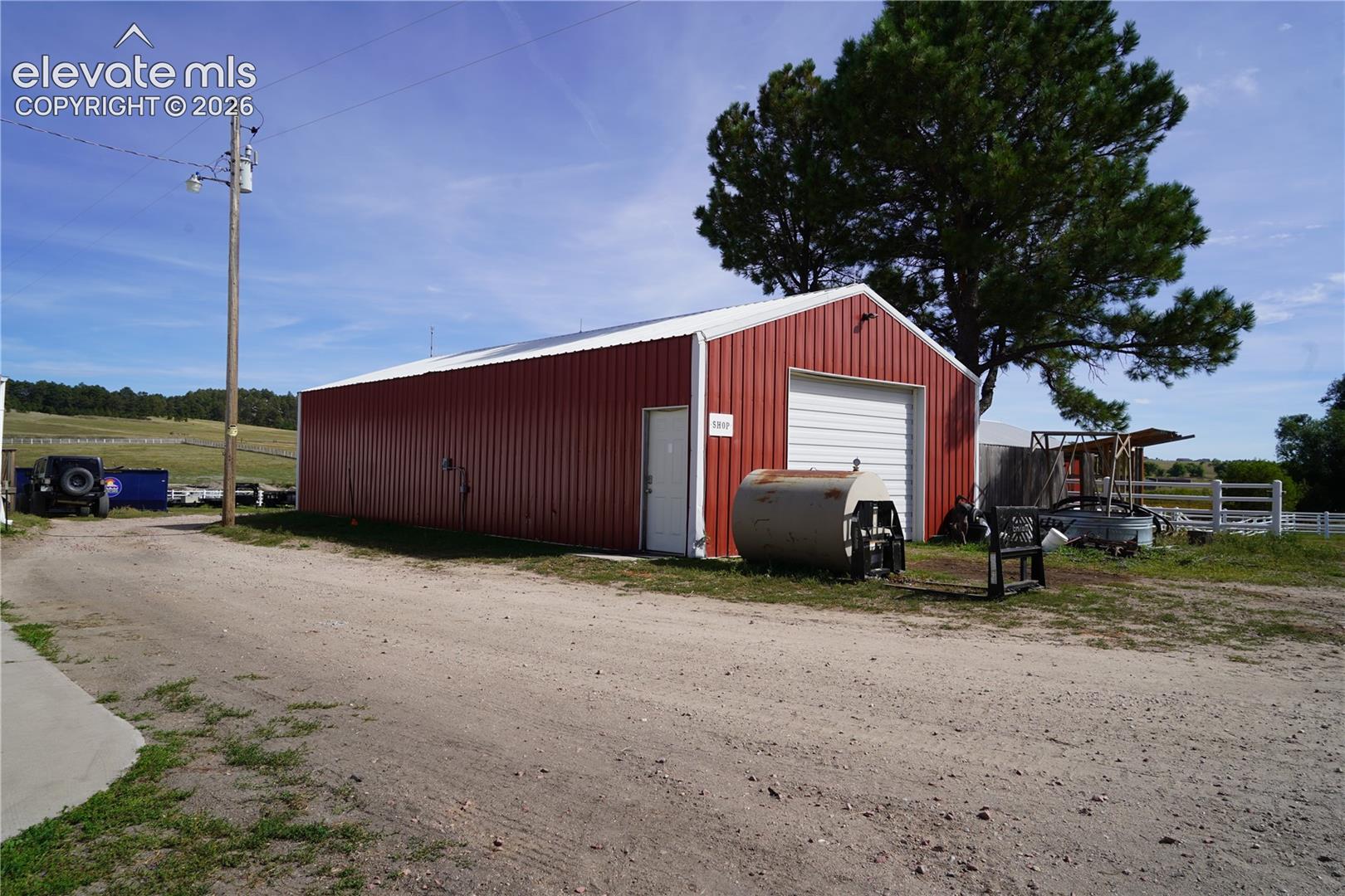 Red metal building with white trim, a roll-up garage door, and a single entry door