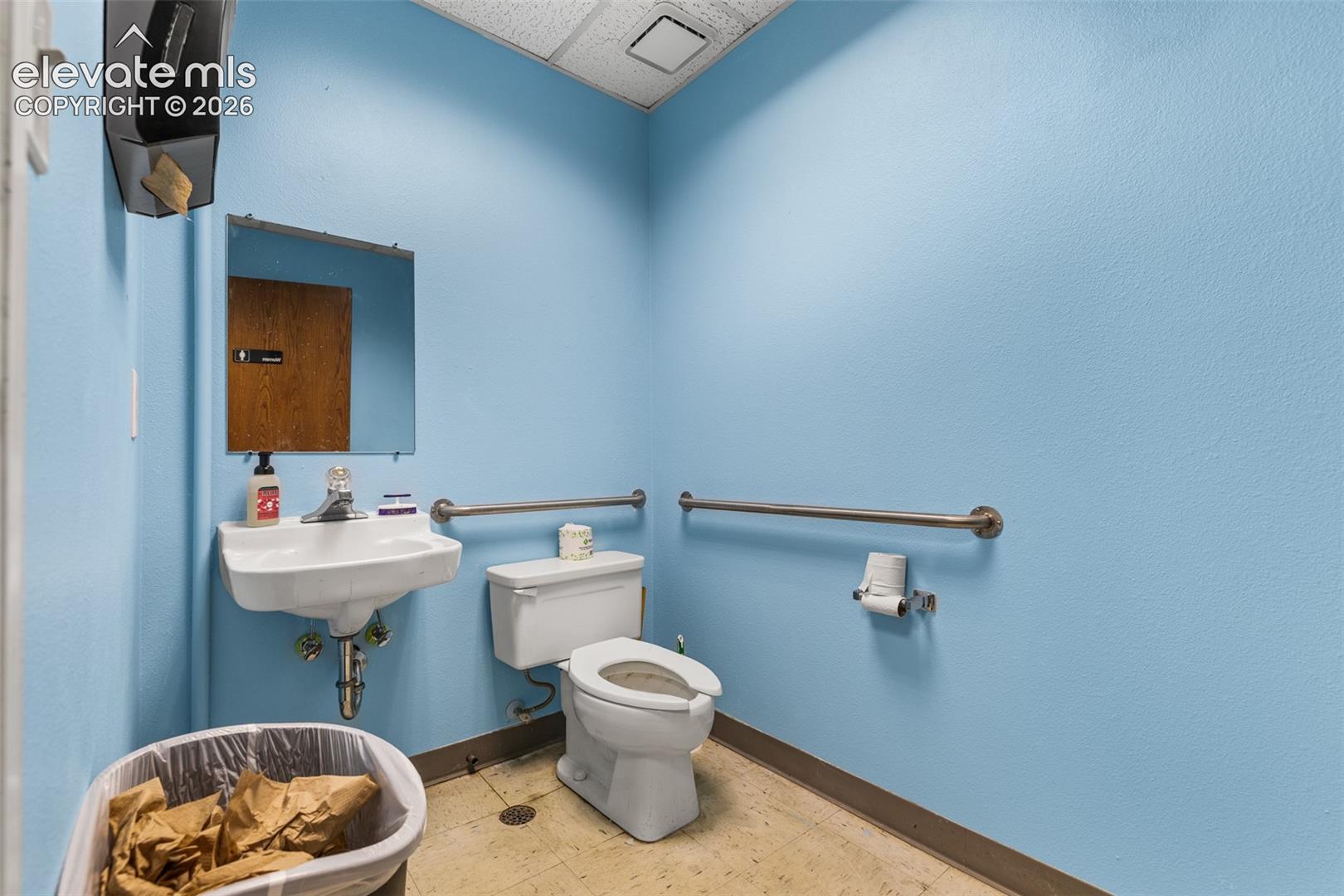Wall-mounted porcelain sink with single-handle faucet, white elongated toilet, and stainless steel grab bars