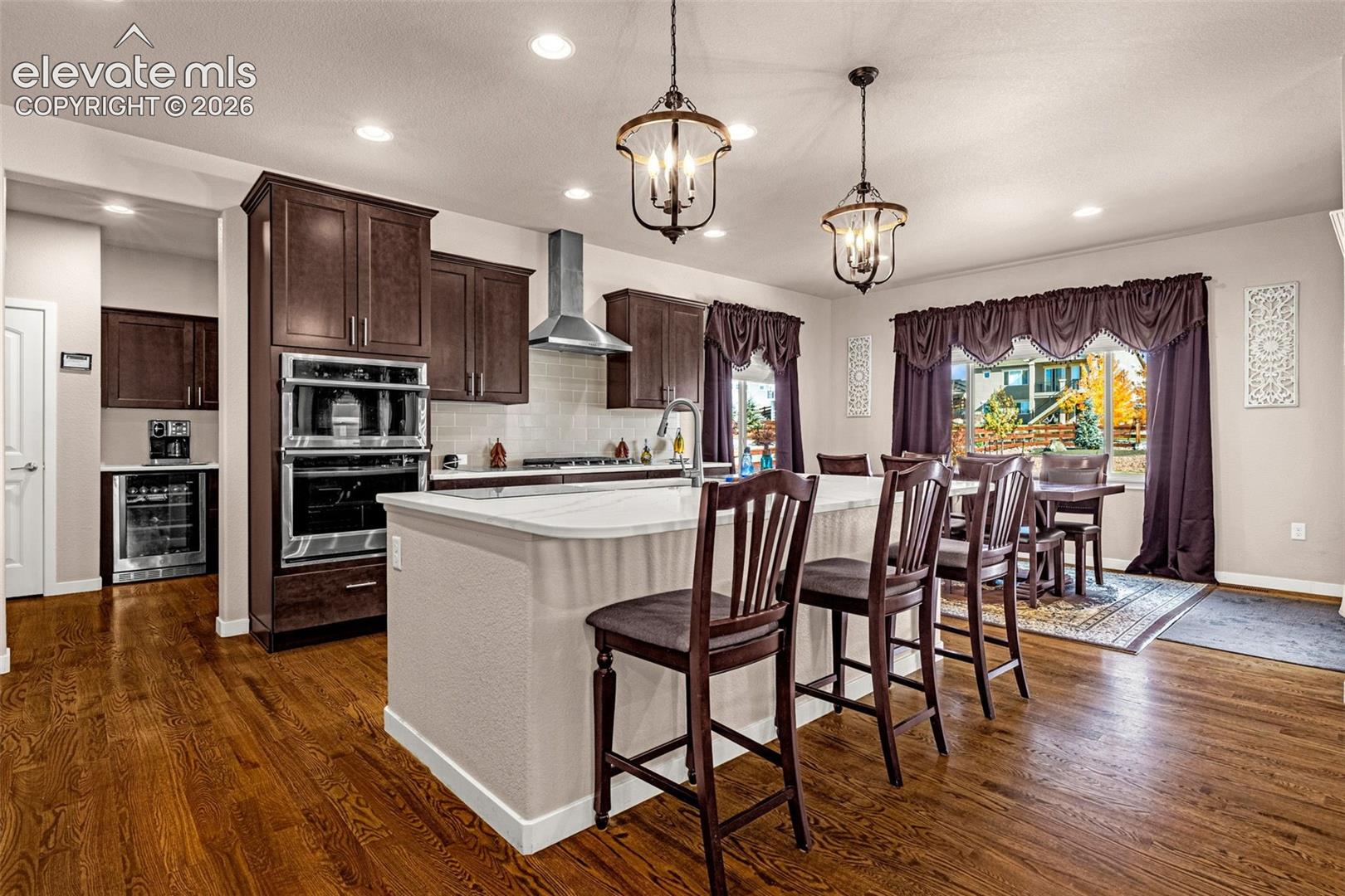 Kitchen featuring a central island with a solid-surface countertop, dark wood cabinetry, double wall ovens, stainless steel range hood, and recessed lighting
