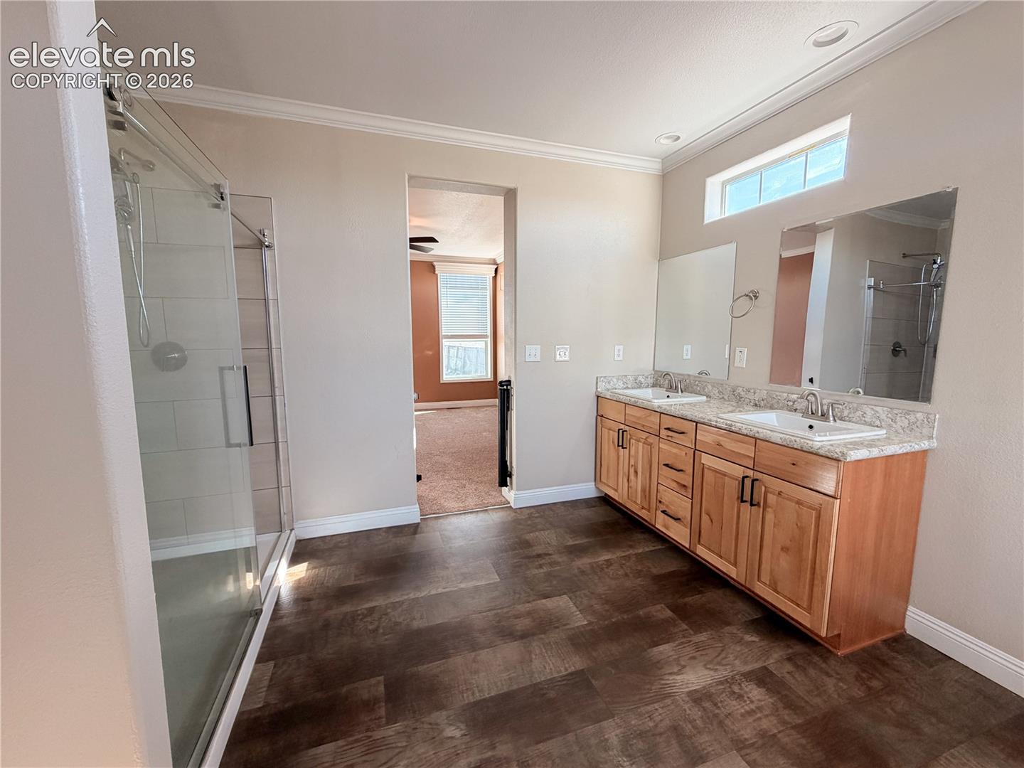 Dual-sink vanity with stone-finish countertop, wood-finish cabinetry, walk-in glass-enclosed shower, transom window, and recessed ceiling lighting