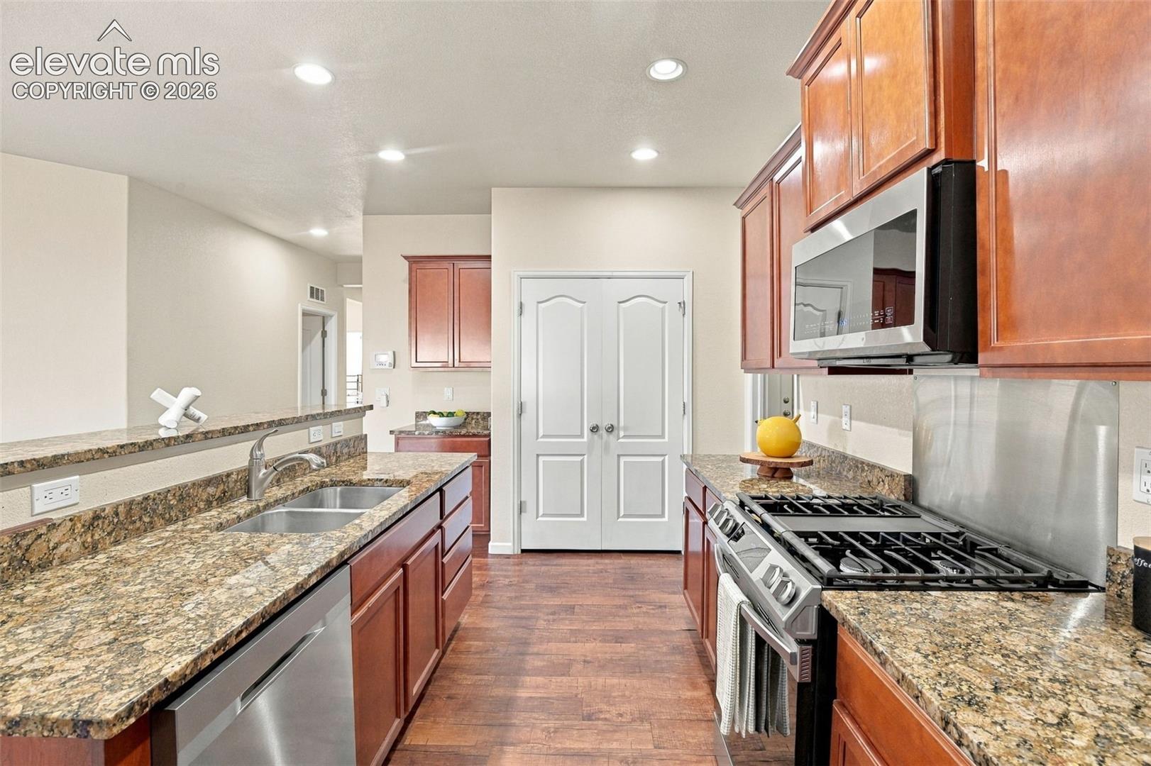 Kitchen featuring stained wood cabinetry, stone-surface countertops, stainless steel appliances including a gas range and built-in microwave, wood-finish flooring, and recessed lighting