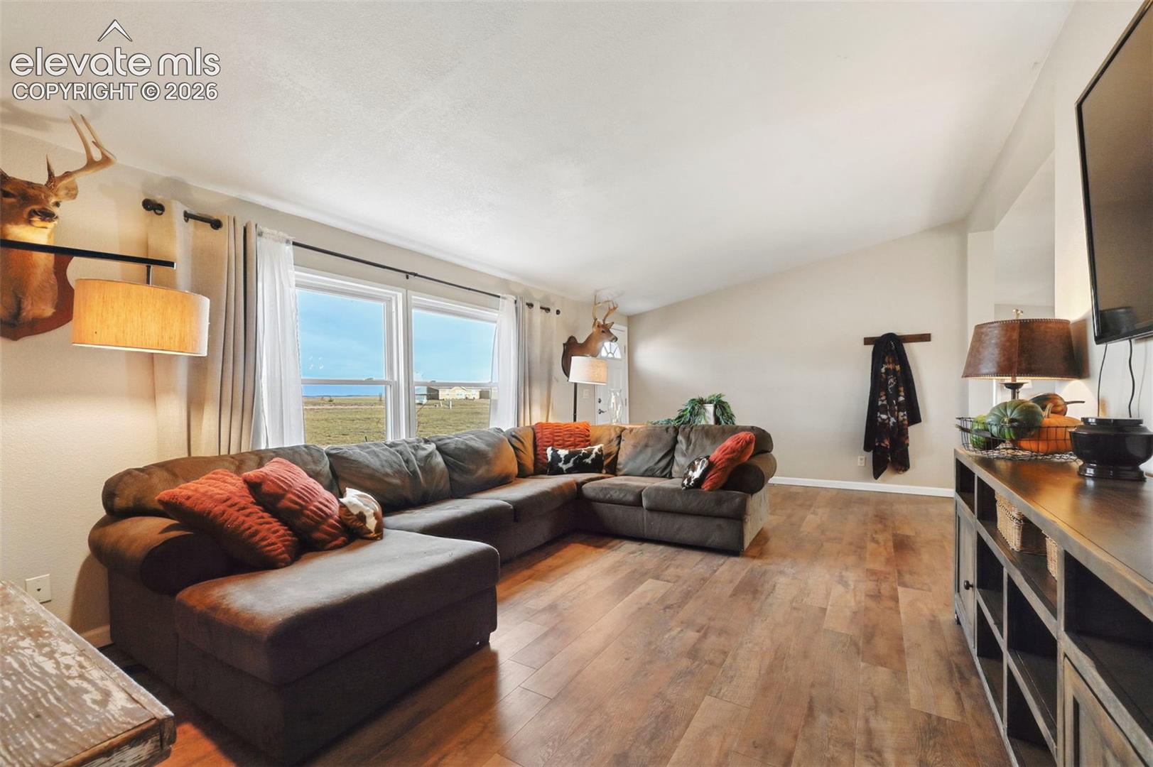 Living area featuring vaulted ceilings, wood-finish flooring, and expansive windows