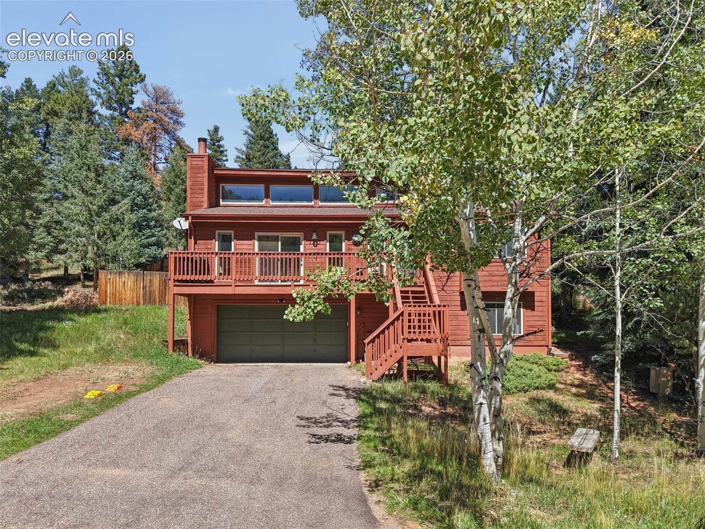 Wood-sided exterior with an attached deck, upper-level transom windows, a prominent chimney, and a ground-level garage door