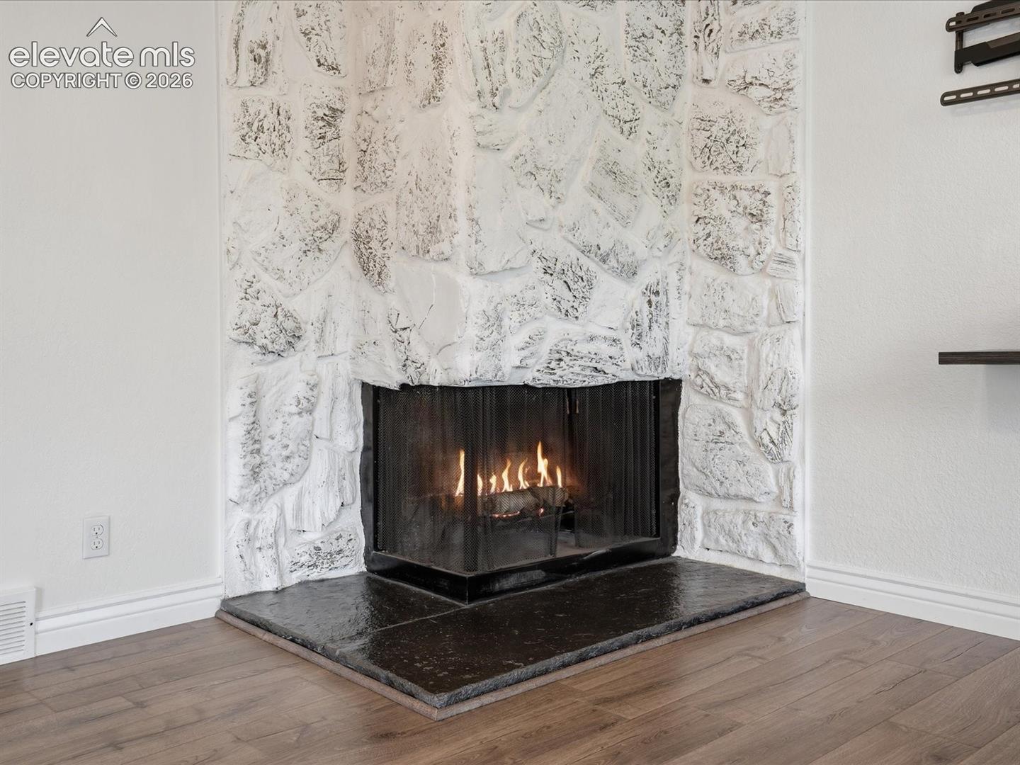 Corner fireplace featuring a floor-to-ceiling white stone surround, metal fire screen, and a dark stone hearth, finished with wood-finish flooring
