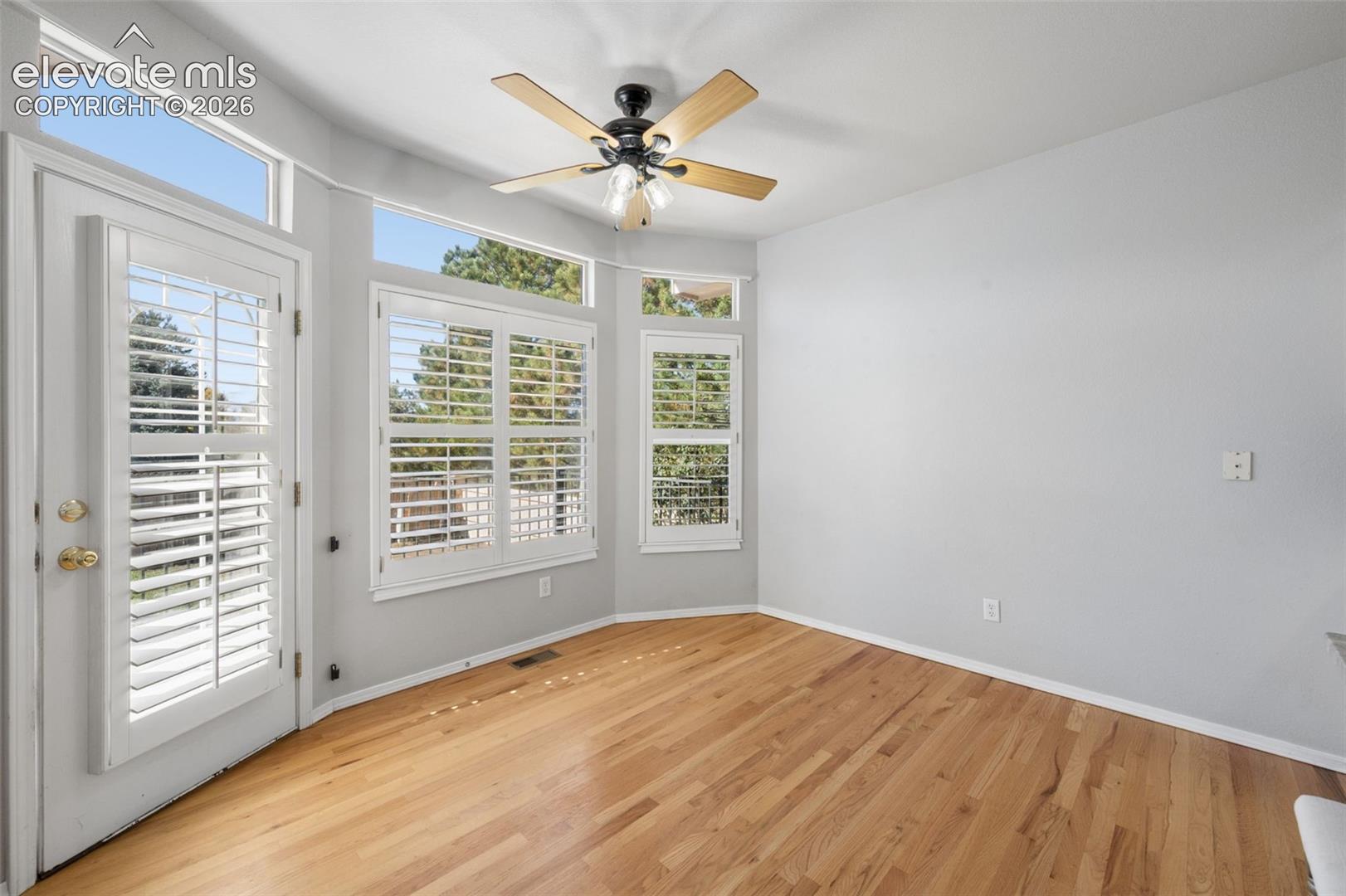 Room featuring wood-finish flooring, plantation shutters, transom windows, and a ceiling fan with integrated lighting