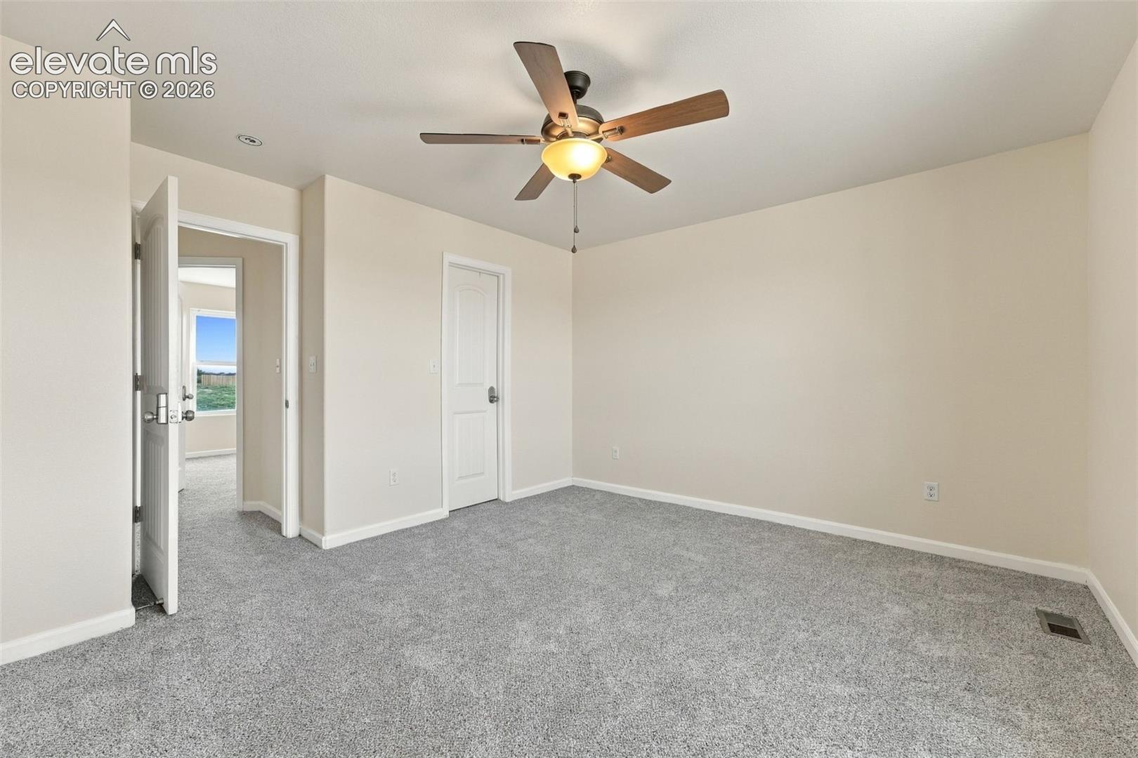 Neutral-toned room featuring neutral wall-to-wall carpeting, a multi-blade ceiling fan with an integrated light fixture, and two-panel interior doors