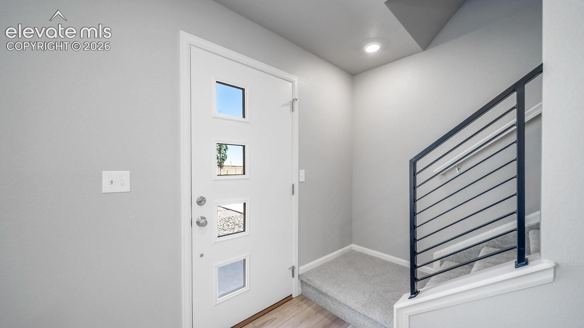 Entryway featuring a solid white door with four square glass inserts, light-toned wood-finish flooring, and a staircase with a modern horizontal metal railing
*photos of a model home*
