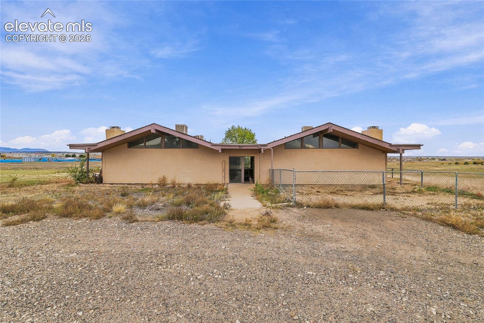 Mid-century modern exterior featuring a dual-gabled roofline, stucco siding, large triangular clerestory windows, and a paved walkway