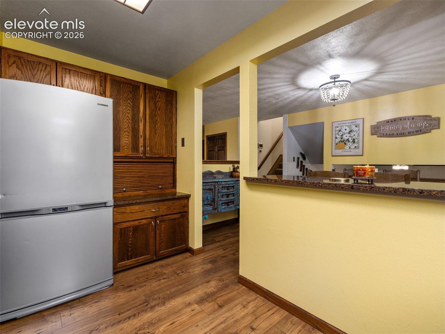 Wood-finish flooring with built-in wood cabinetry, a stainless steel refrigerator, and a breakfast bar with a decorative light fixture